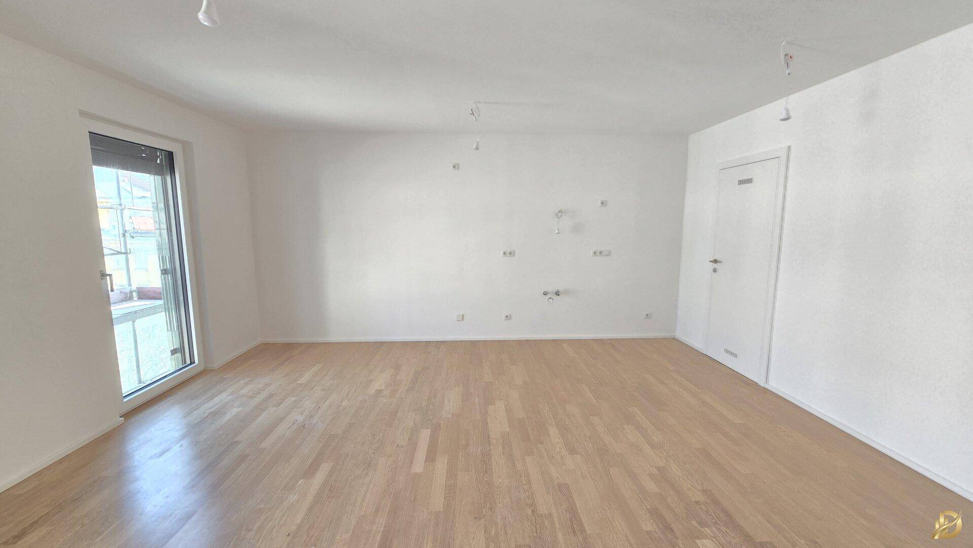 Helles Zimmer mit Parkettboden und einer Tür, die zu einem weiteren Raum führt.