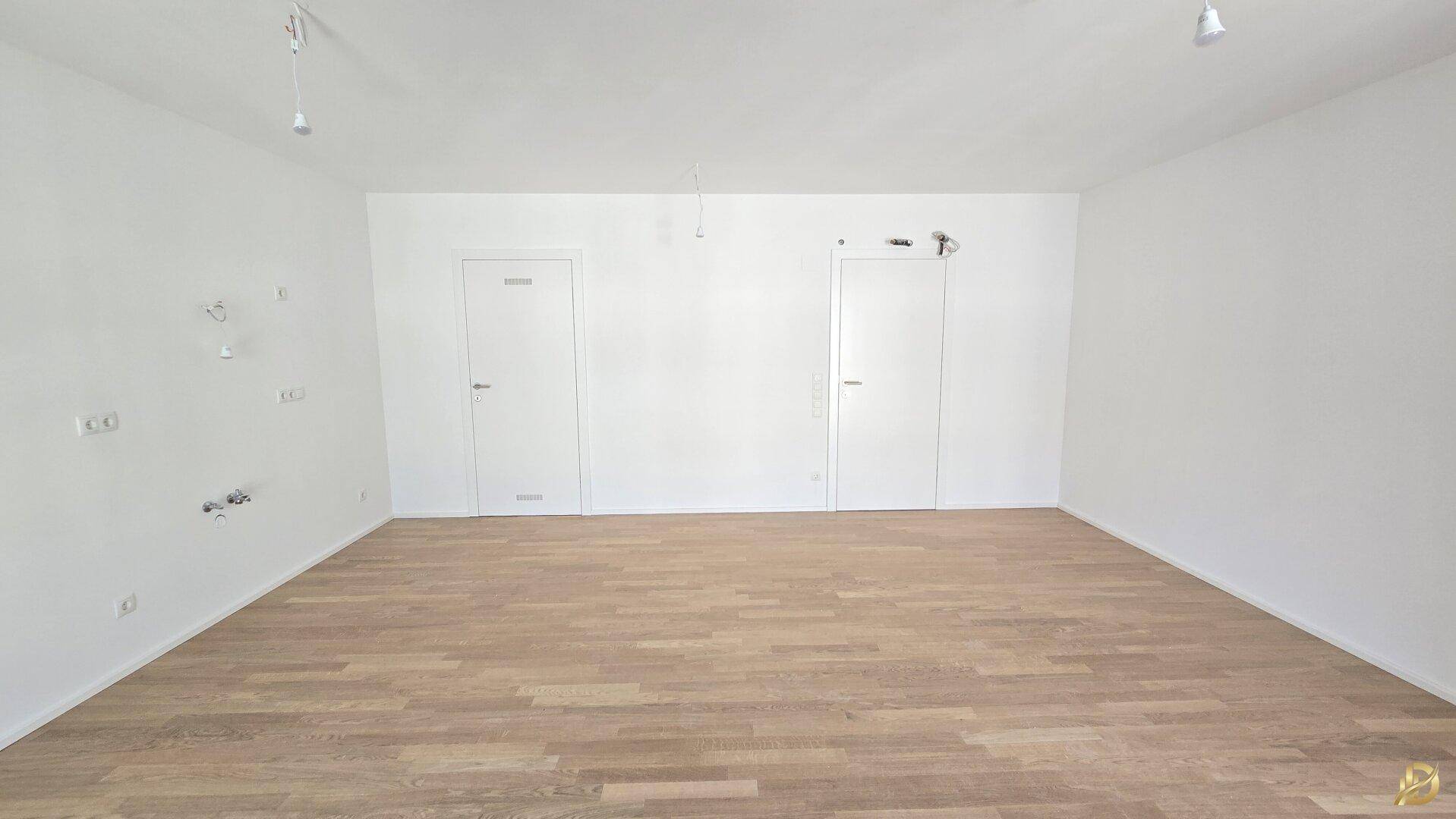 Geräumiges Zimmer mit hellem Parkettboden und zwei weißen Türen, bietet eine klare Raumstruktur.