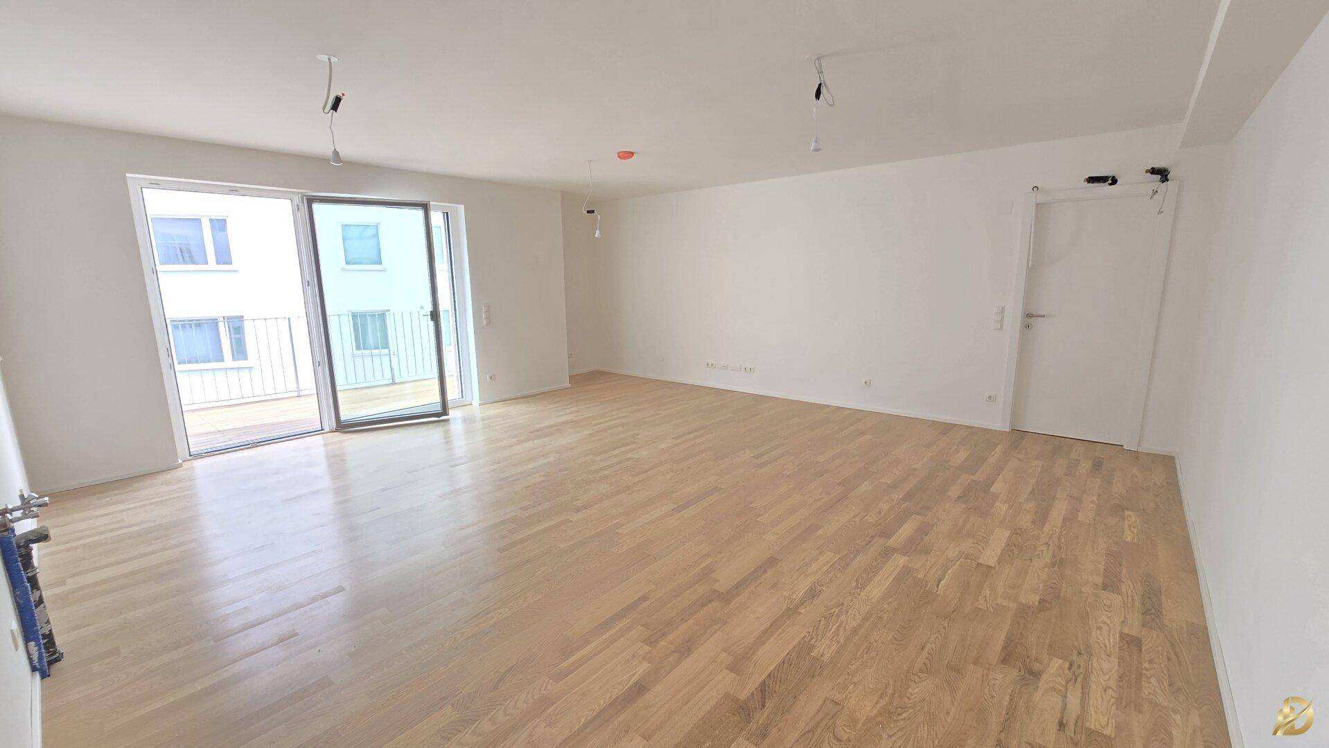 Heller, leerer Wohnraum mit Eichenparkettboden und Zugang zu einem Balkon oder einer Terrasse.
