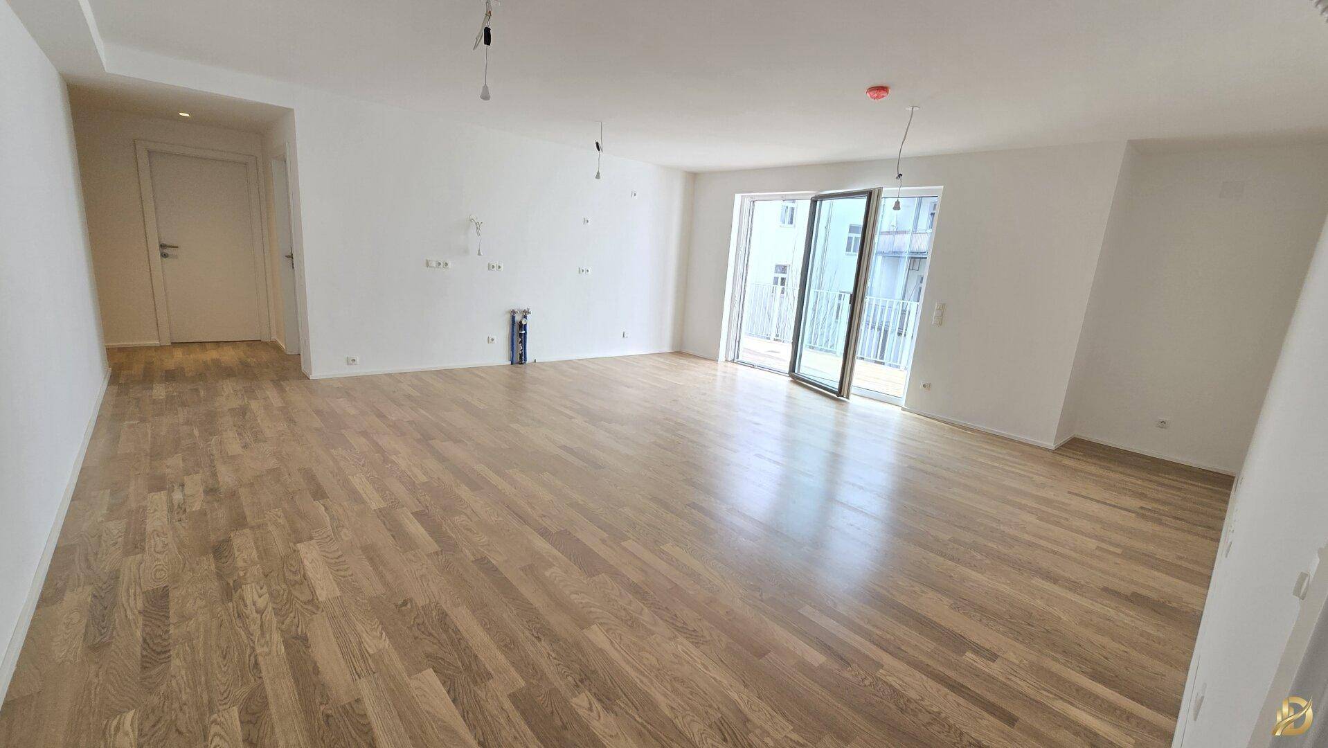 Großer, heller Wohnbereich mit Parkettboden und Zugang zu einem Außenbereich durch Glasschiebetüren.