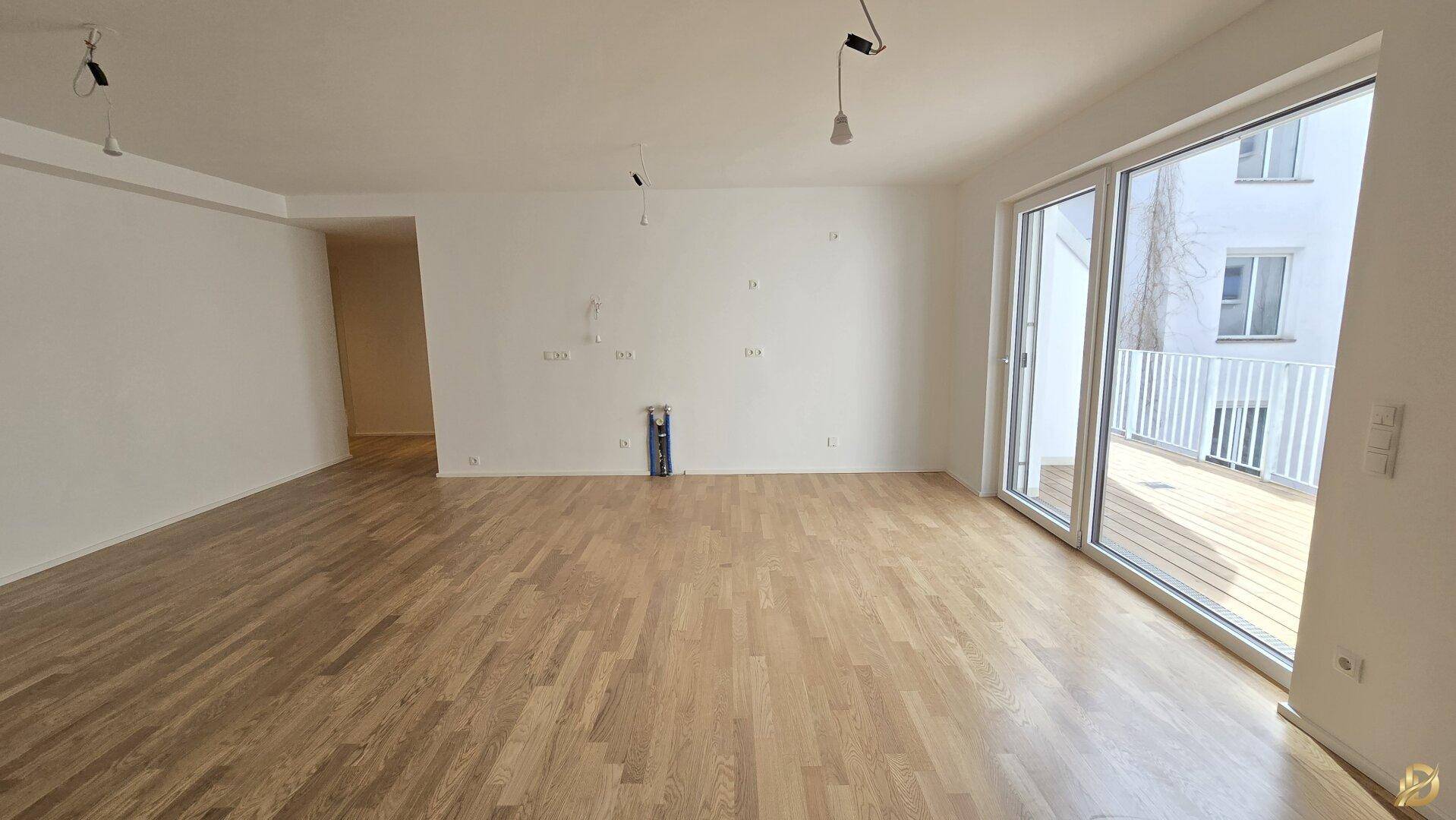 Lichtdurchfluteter Wohnraum mit hellem Parkettboden und breiten Glasschiebetüren zu einem Balkon.