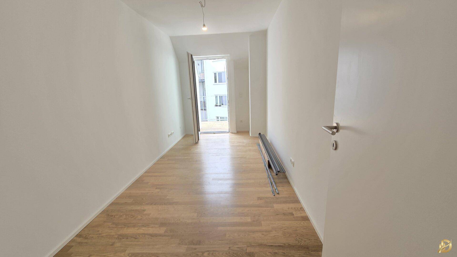 Helles Zimmer mit Parkettboden und Zugang zu einem Balkon, ideal als Schlafzimmer.