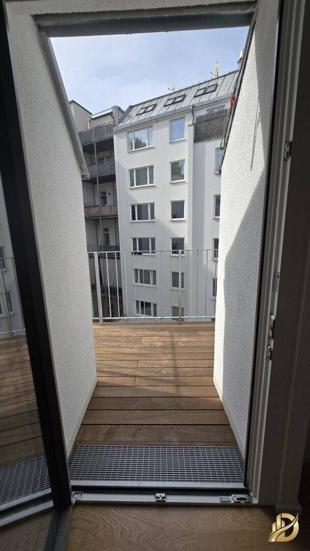 Blick von innen auf eine Holzterrasse mit Metallgeländer und die umliegenden Gebäude.