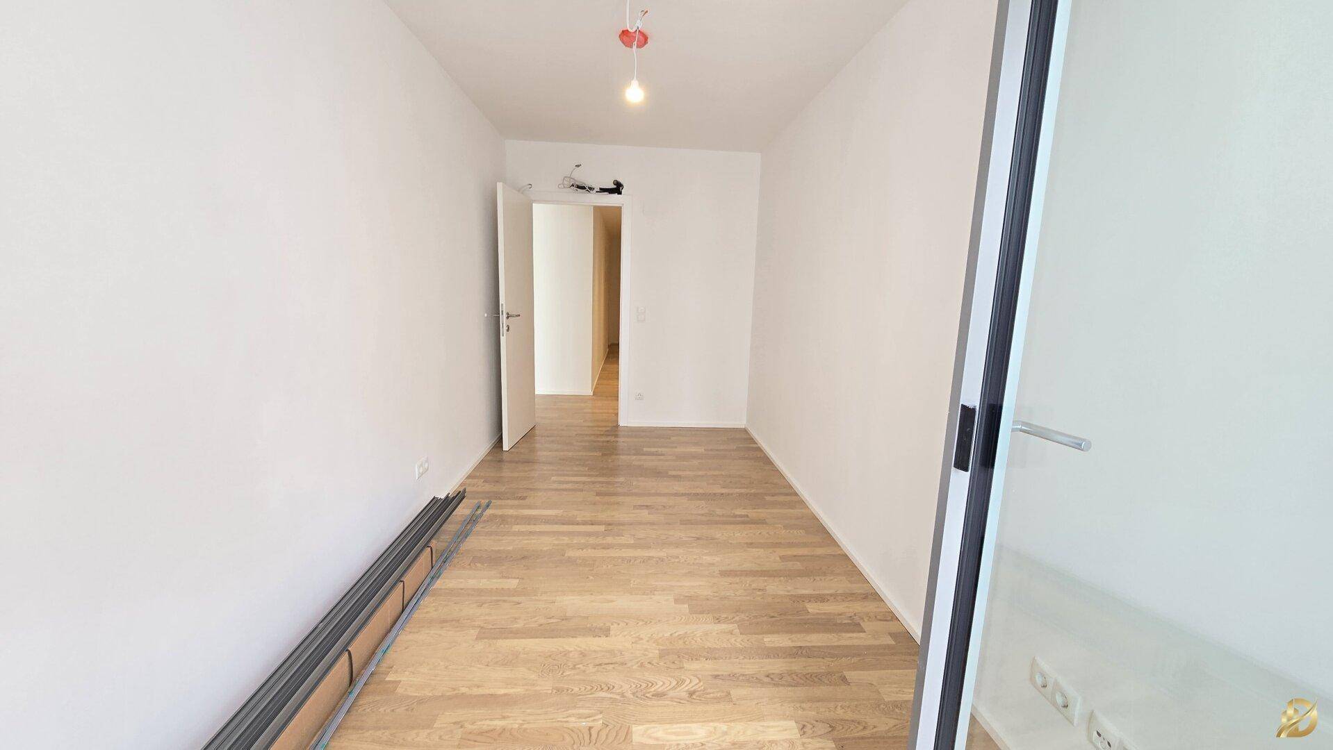 Helles Zimmer mit Parkettboden und Glasschiebetür, geeignet als Schlaf- oder Gästezimmer.