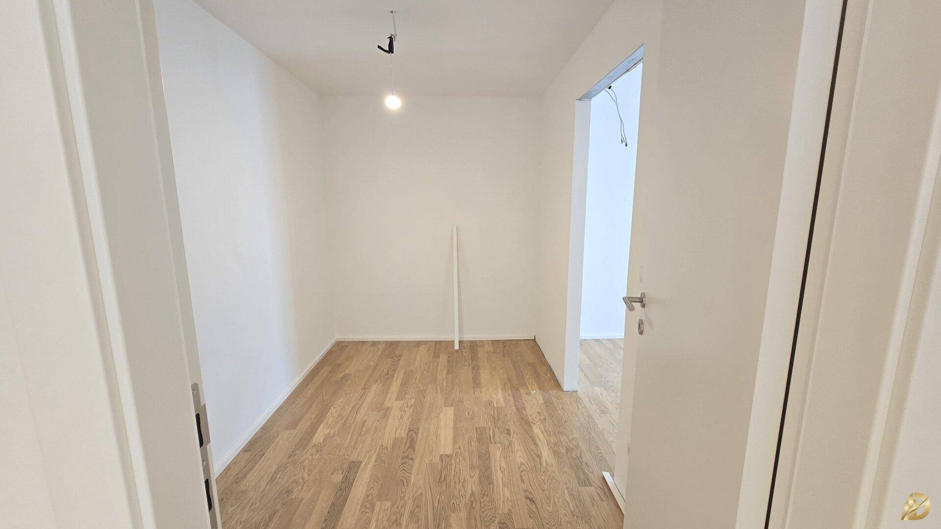 Helles Zimmer mit Parkettboden und weißen Wänden, bietet Zugang zu einem weiteren Raum.