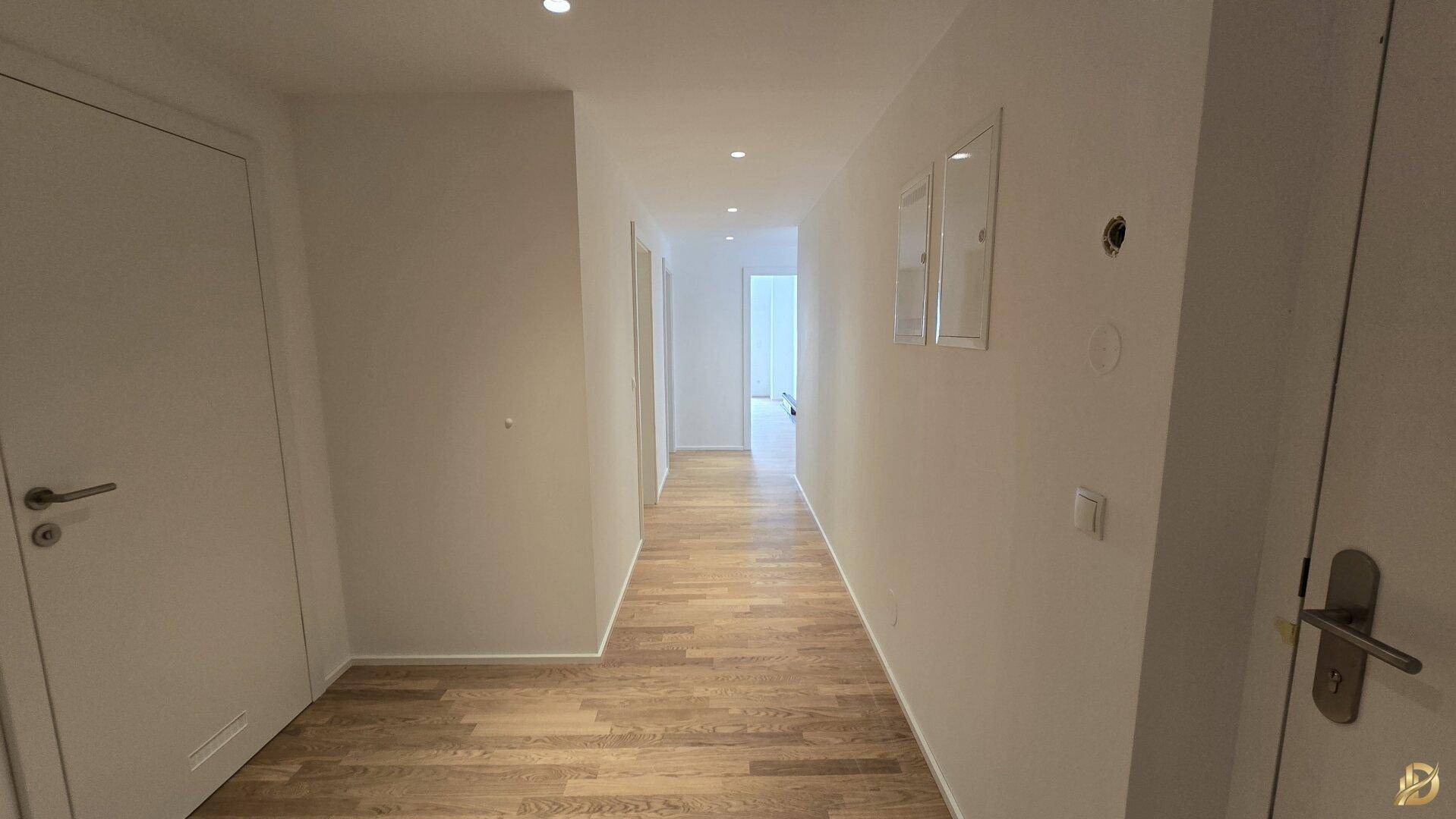 Langer, heller Flur mit Parkettboden und integrierter Deckenbeleuchtung.