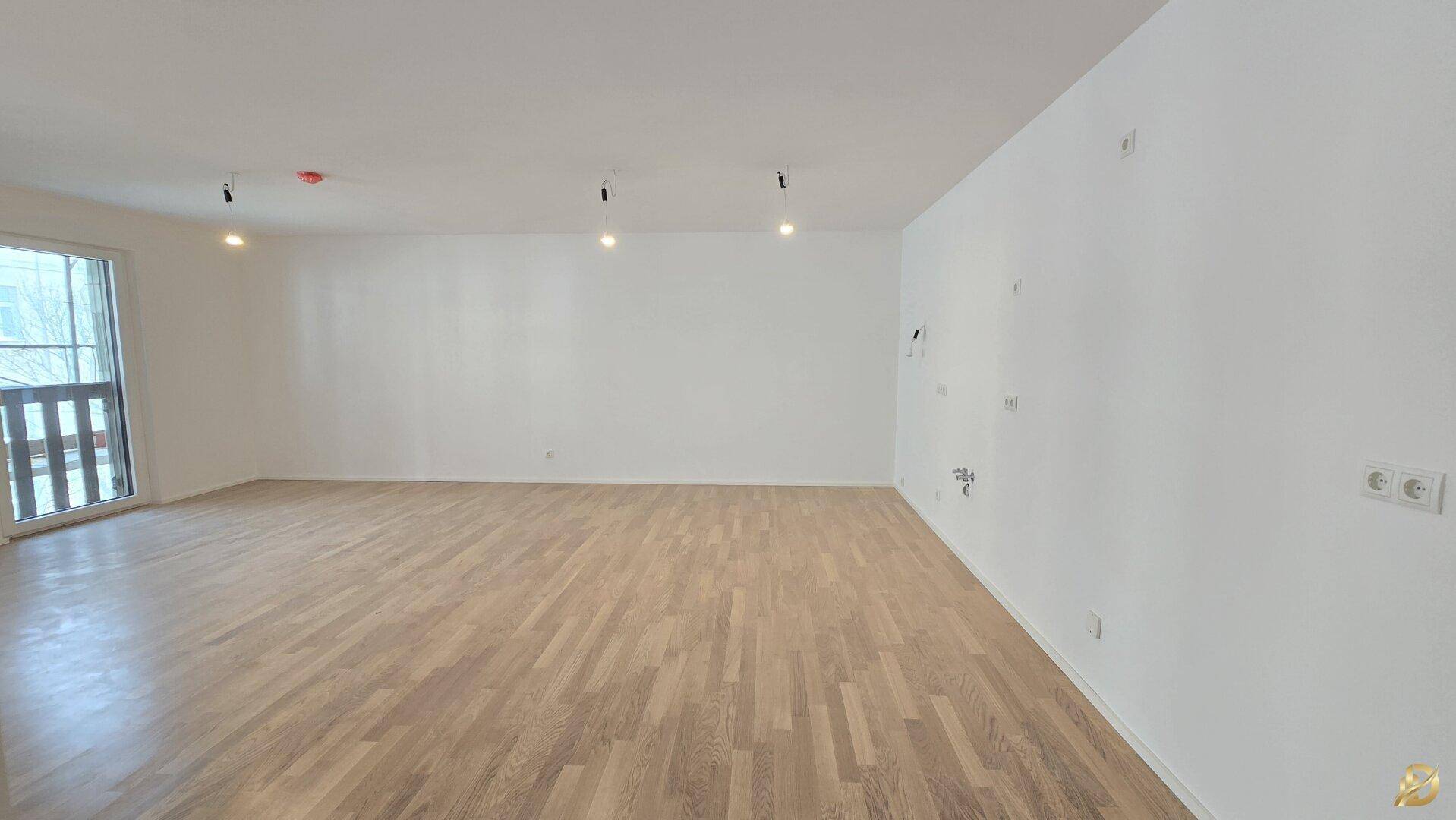 Großer, heller Raum mit neuem Parkettboden und Zugang zu einem Balkon.