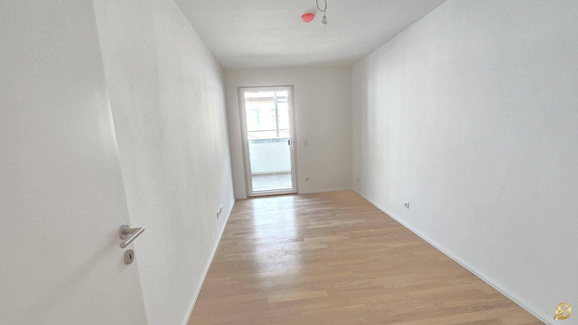 Helles Schlafzimmer mit Parkettboden und Zugang zu einem kleinen Balkon.