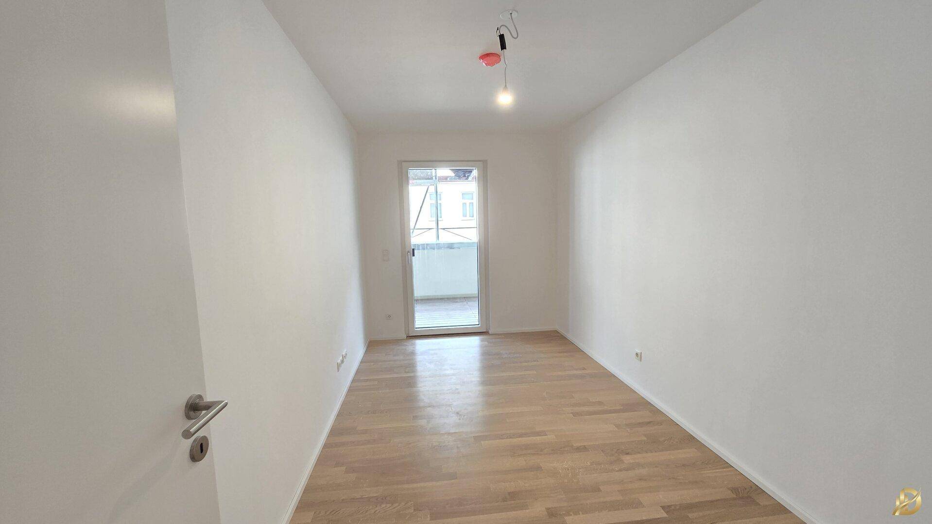 Helles Schlafzimmer mit Parkettboden und Zugang zu einem kleinen Balkon.