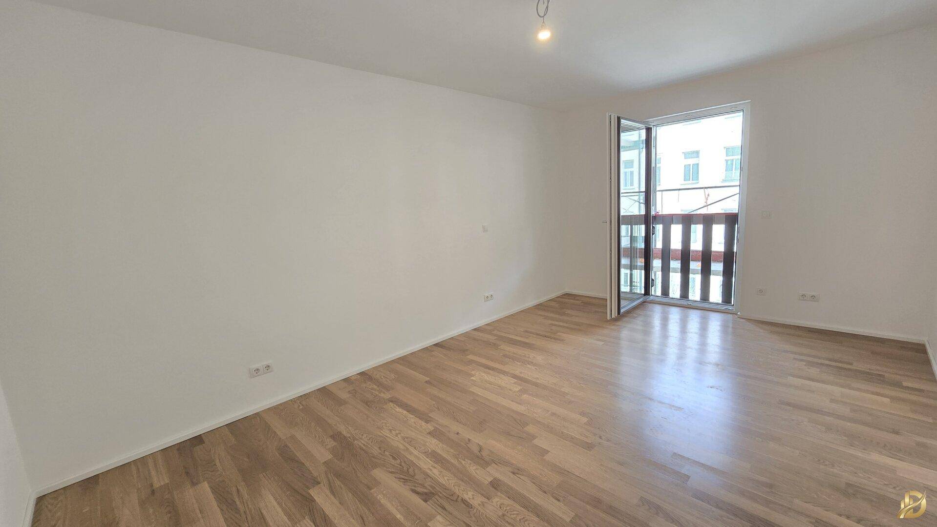 Helles Schlafzimmer mit Parkettboden und Zugang zu einem kleinen Balkon.