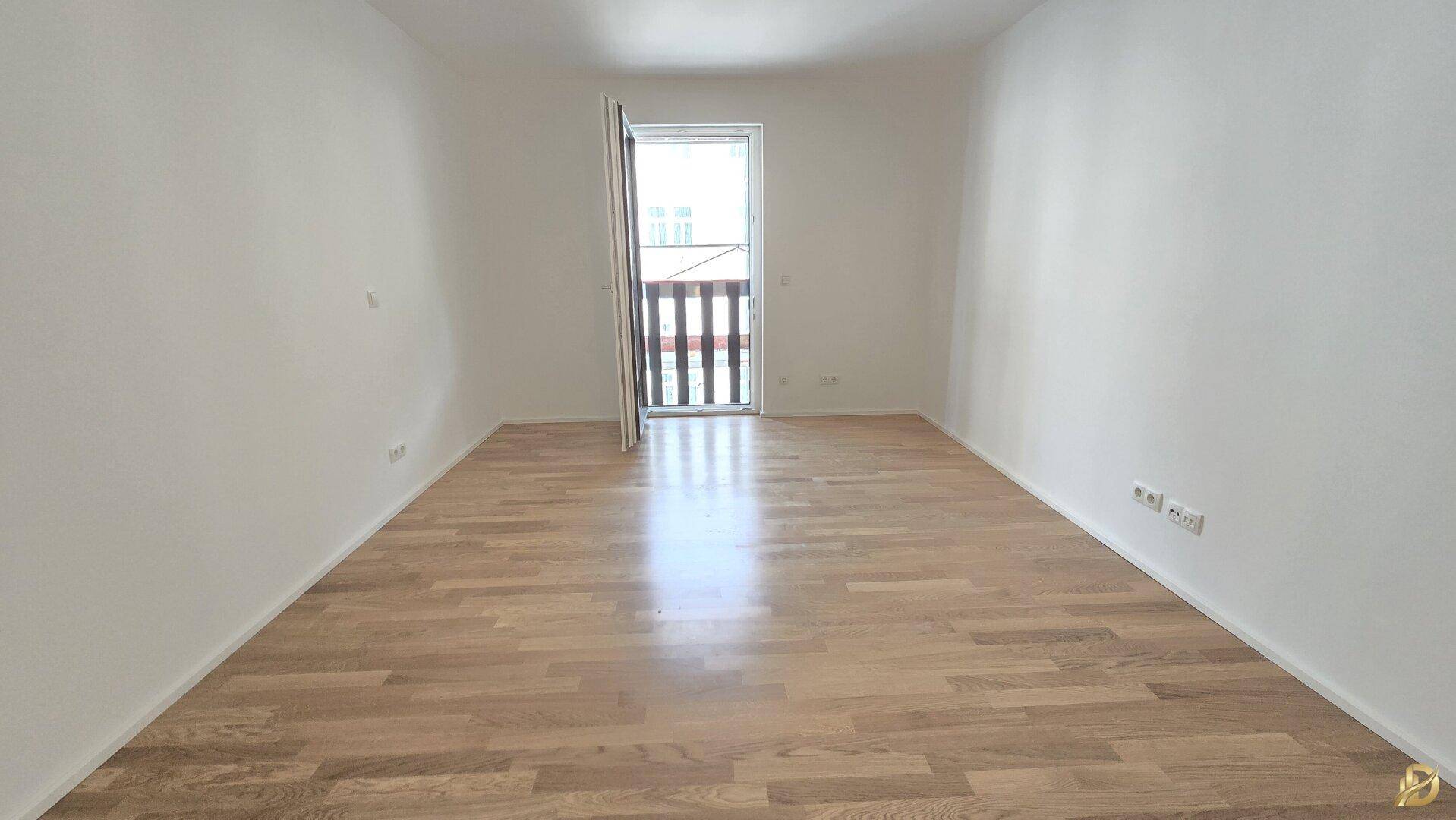 Helles Schlafzimmer mit Parkettboden und Zugang zu einem kleinen Balkon.