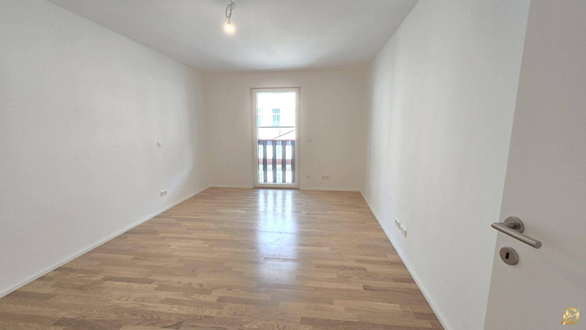 Helles Schlafzimmer mit Parkettboden und Zugang zu einem kleinen Balkon.