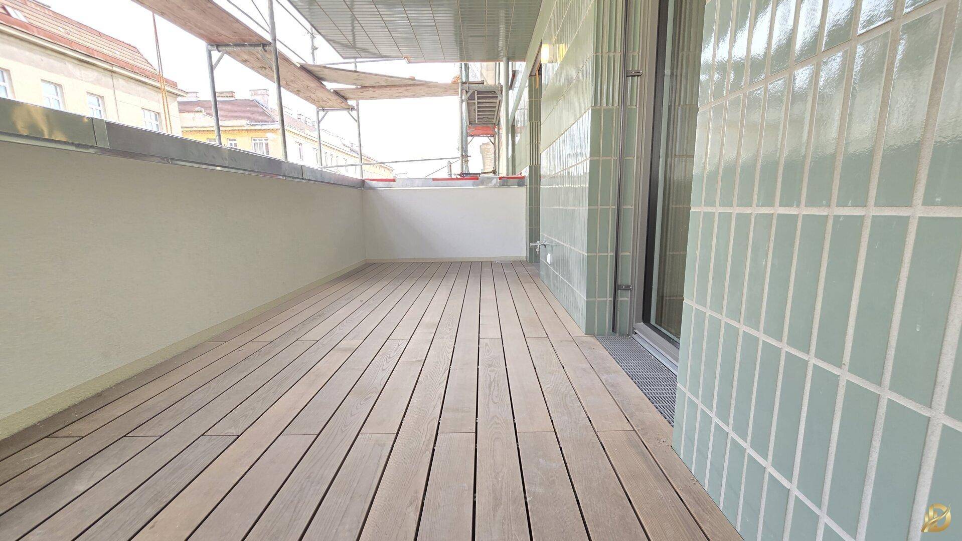 Geräumiger Balkon mit Holzfußboden und modernen Fliesen an der Wand, umgeben von Gerüsten.