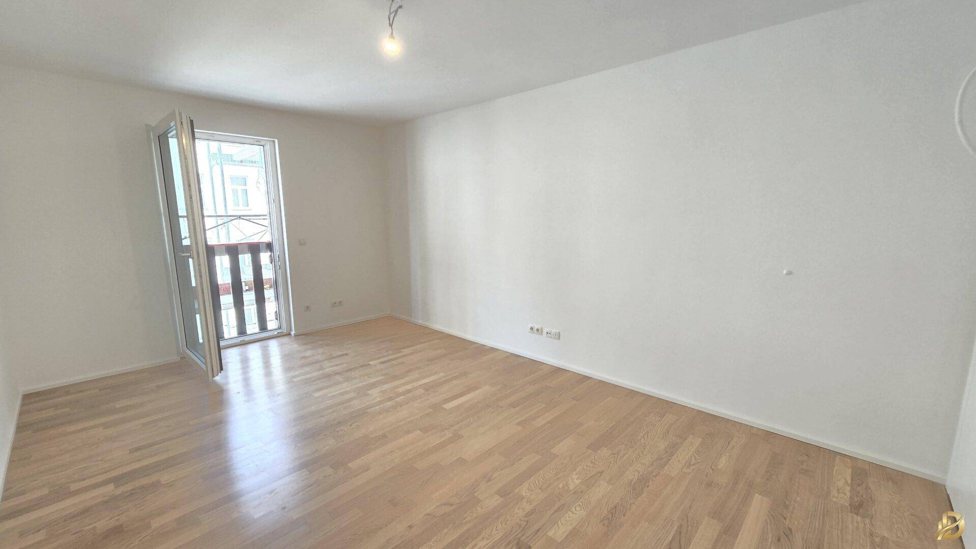 Helles Schlafzimmer mit Parkettboden und Zugang zu einem kleinen Balkon.