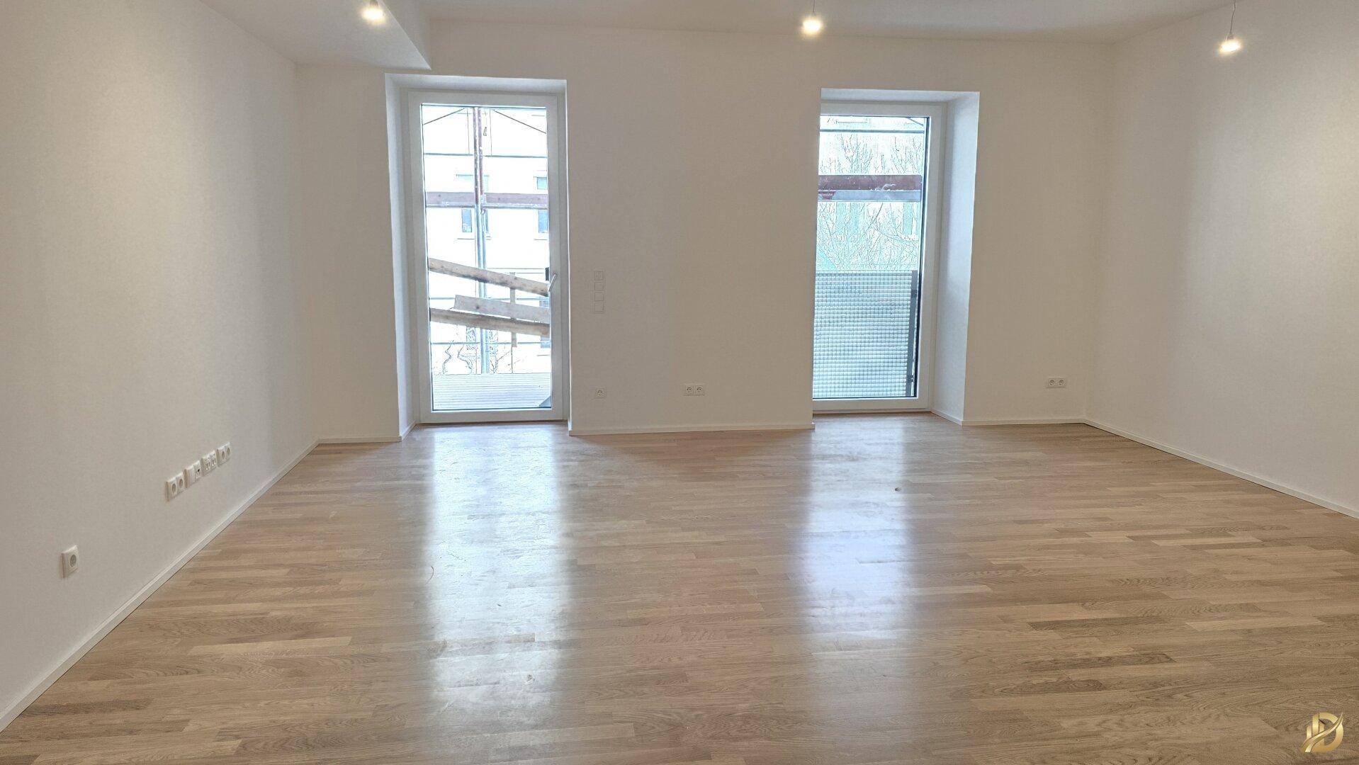Geräumiges Wohnzimmer mit hellem Parkettboden und großen Fenstern.