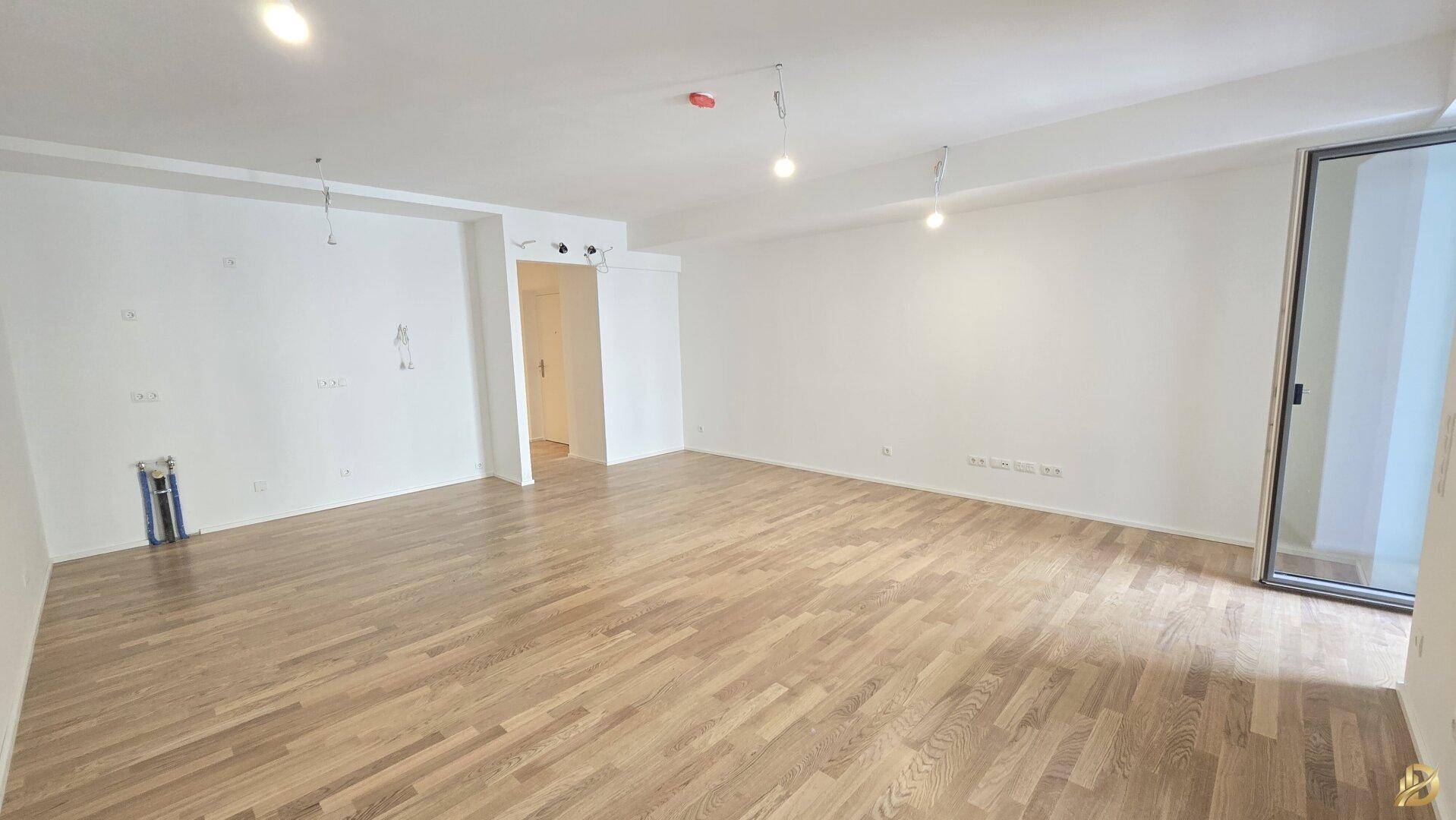 Leeres Wohnzimmer mit Parkettboden und Zugang zu einem Außenbereich.