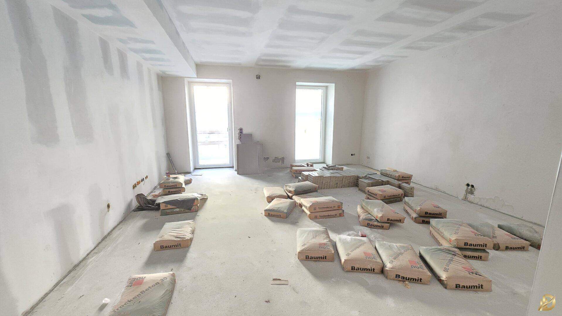 Rohbau eines Zimmers mit Baumaterialien und Fenstern.