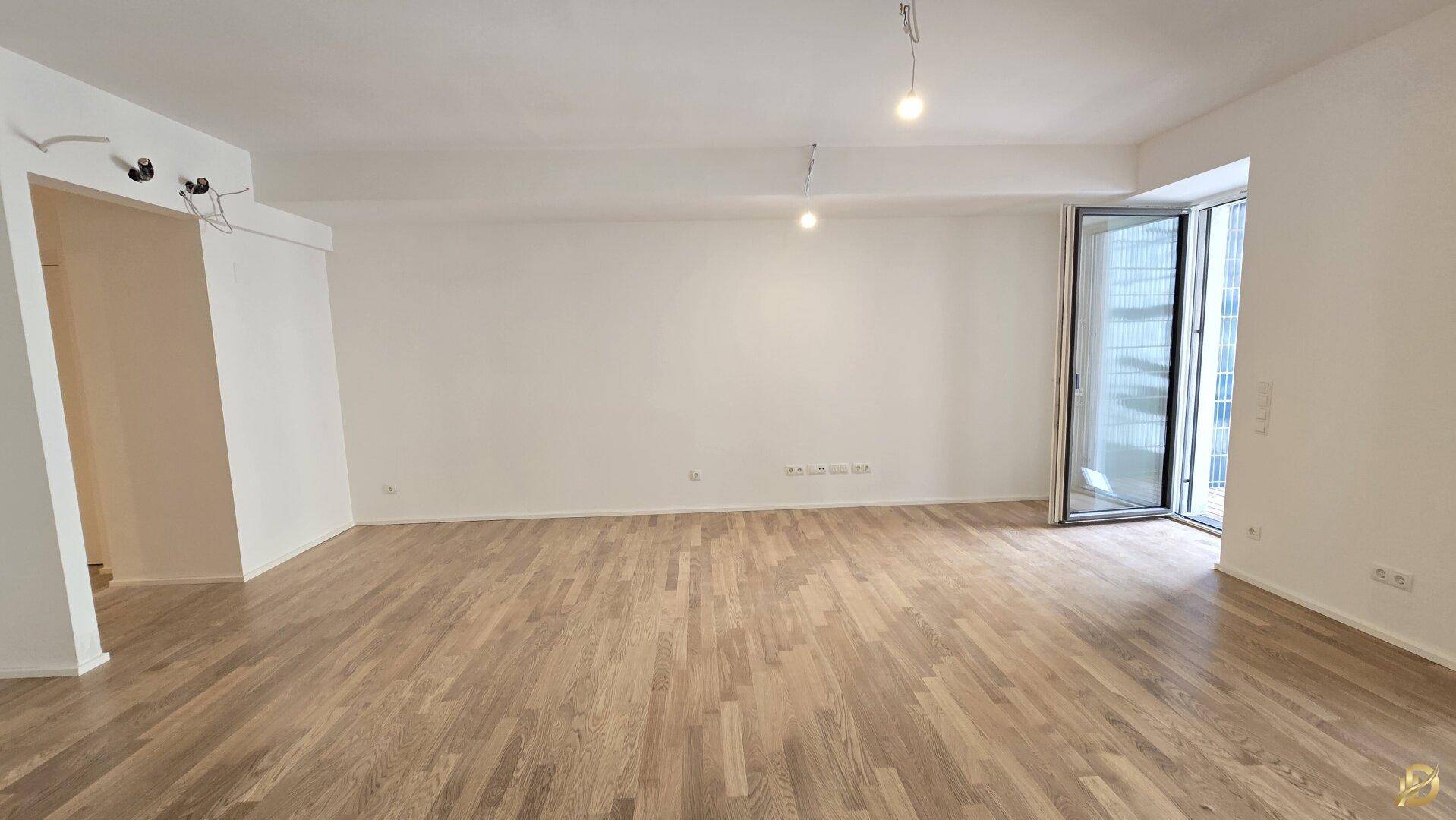 Leeres Wohnzimmer mit Parkettboden und Zugang zu einem Balkon.