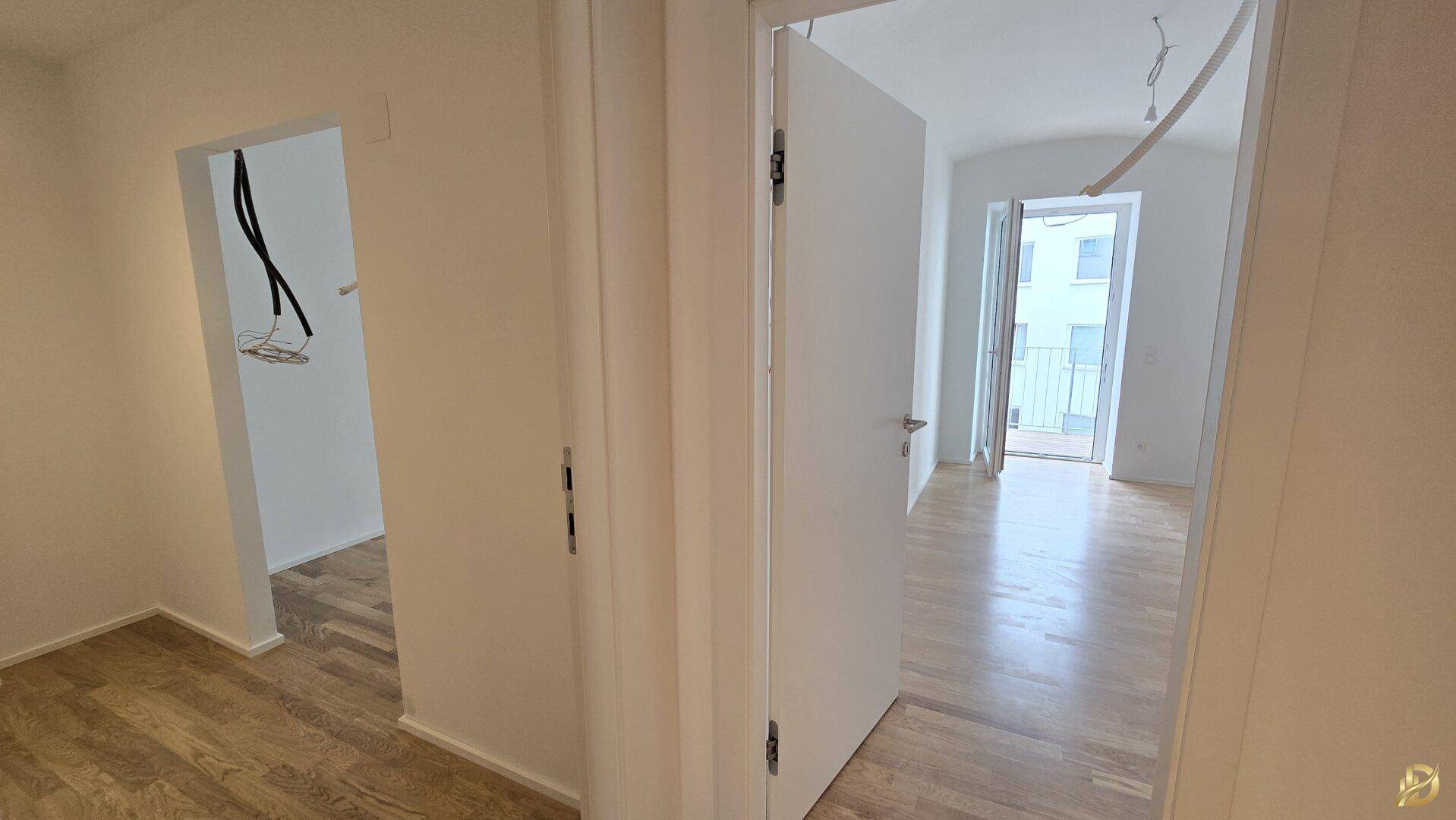 Blick vom Flur in ein helles Zimmer mit Parkettboden und Balkonzugang.