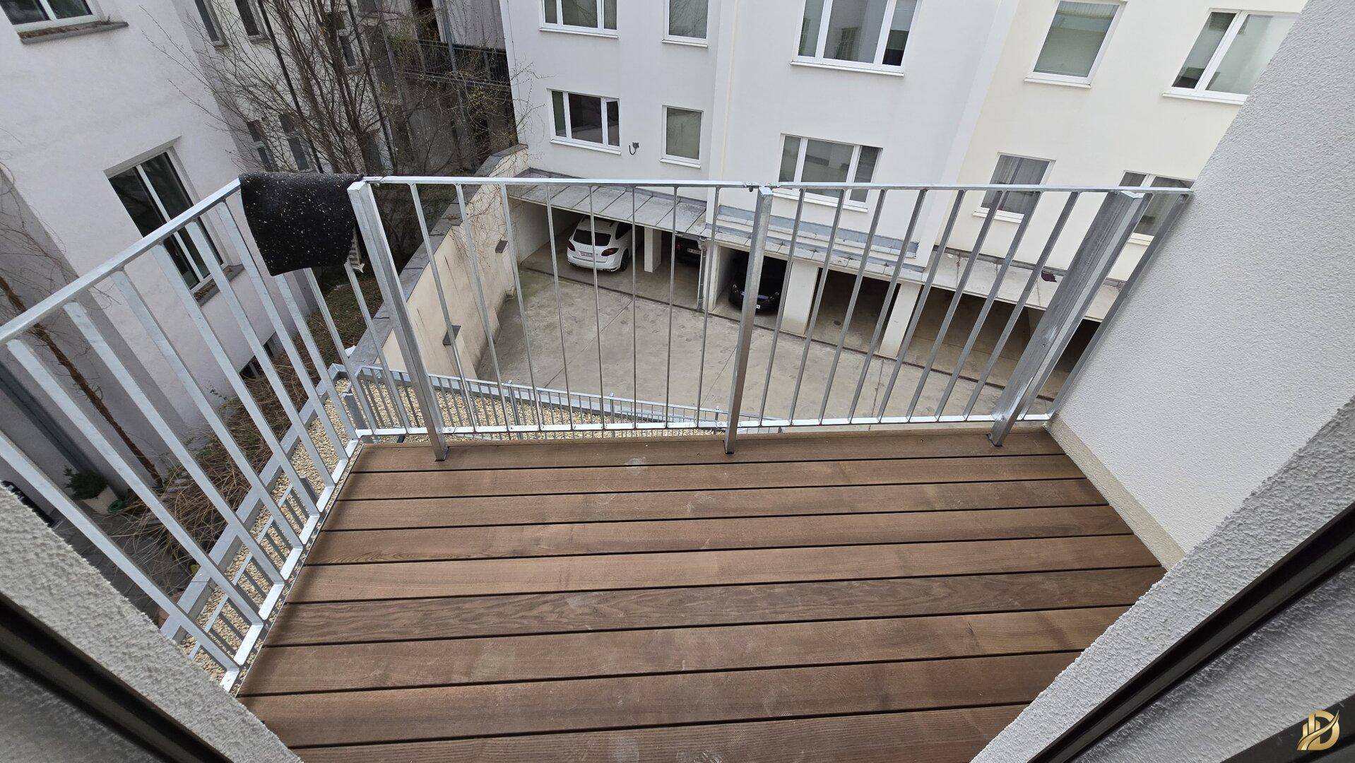 Balkon mit Holzboden und Blick auf den Innenhof mit Tiefgaragenzufahrt.