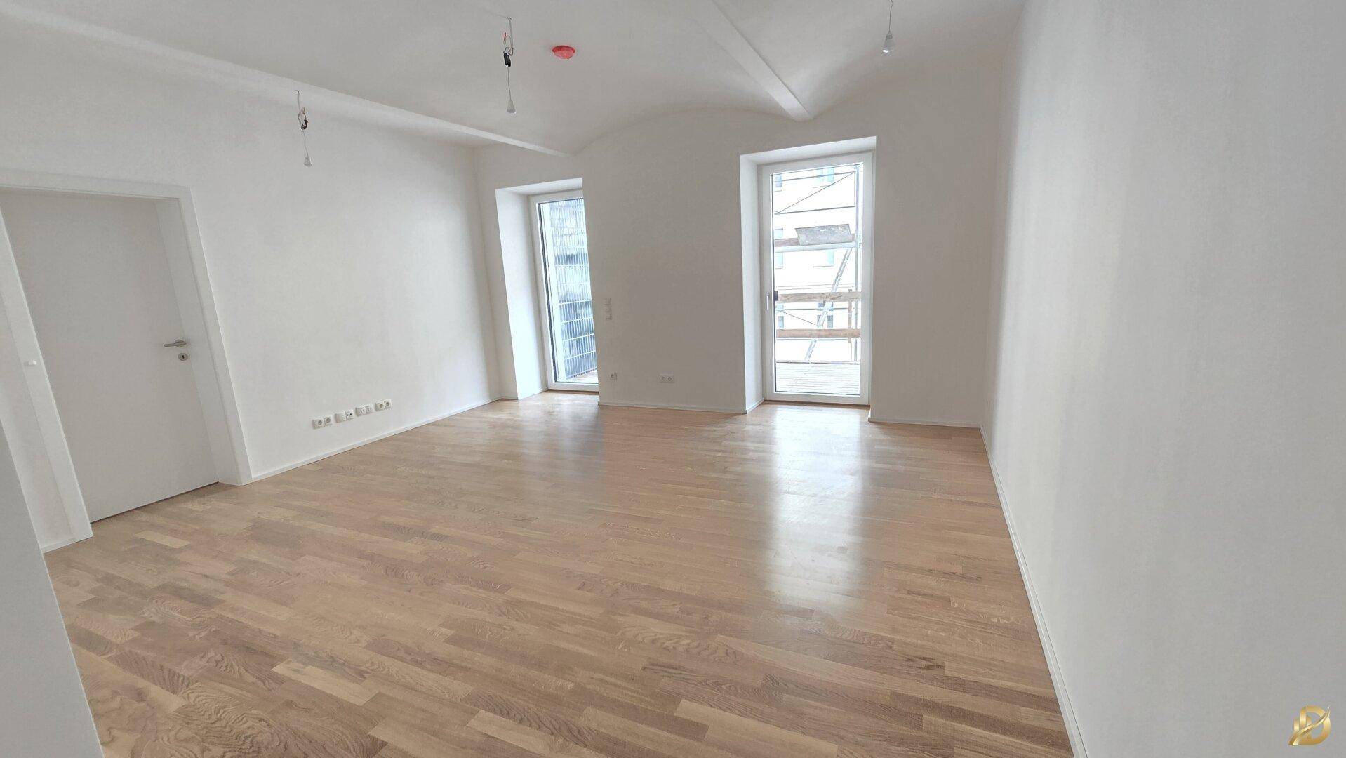Geräumiger, heller Raum mit neuem Holzparkett und großen Fenstern, ideal für ein Wohnzimmer.