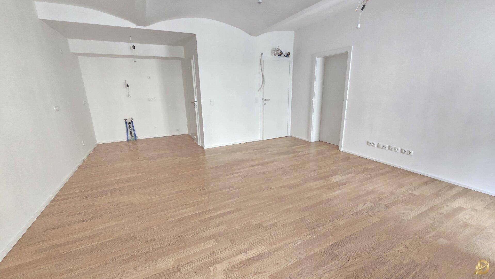 Heller Raum mit Holzparkett und weißen Wänden, vorbereitet für die Installation einer Küche oder eines Hauswirtschaftsraums.