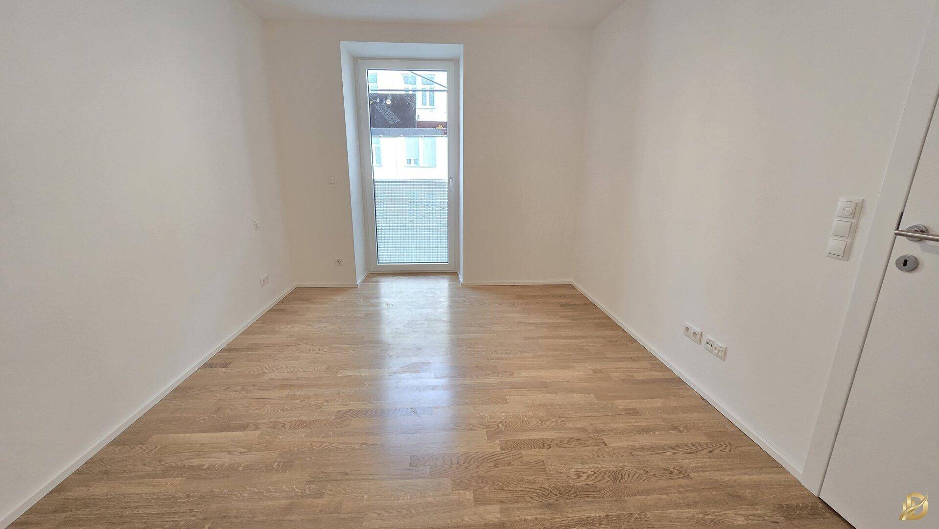 Helles Schlafzimmer mit Holzparkett und einem großen Fenster, bereit für die individuelle Gestaltung.