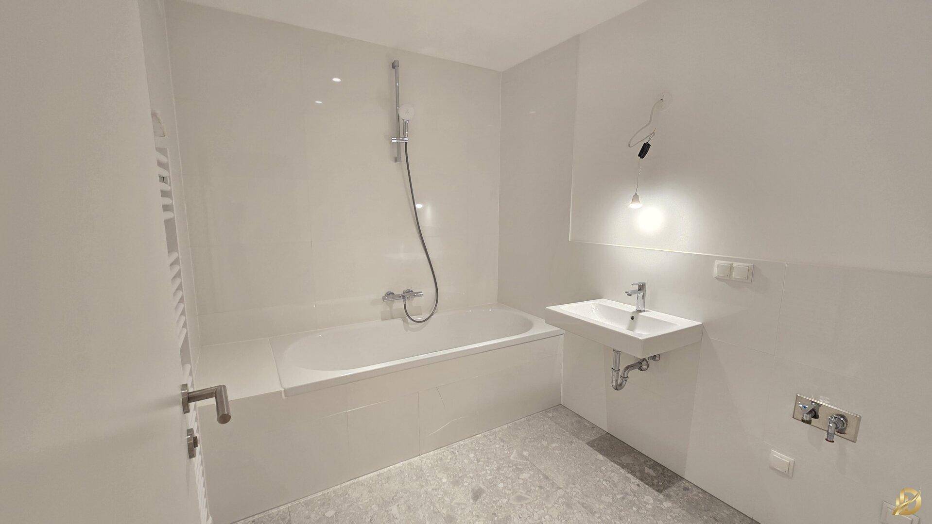 Modernes Badezimmer mit weiß gefliesten Wänden, grauen Bodenfliesen, Badewanne und Waschbecken.