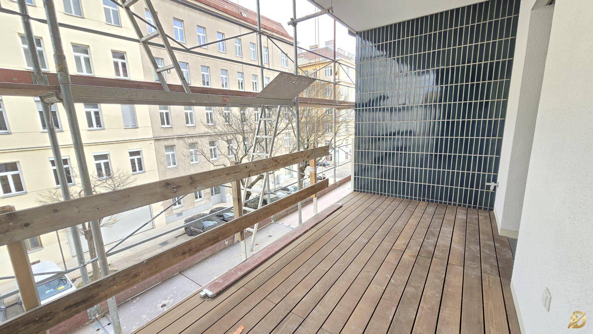 Balkon mit Holzbelag und Blick auf die Straße, umgeben von Baugerüsten.