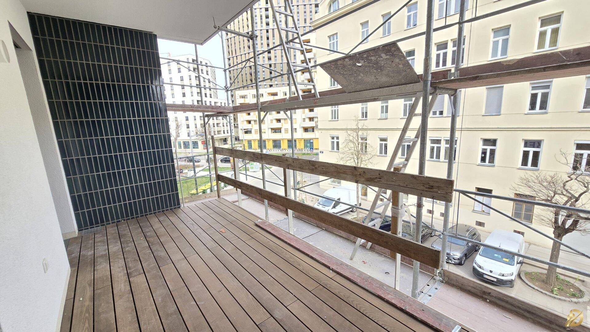Geräumiger Balkon mit Holzfußboden und Blick auf die Umgebung, noch im Bauzustand.