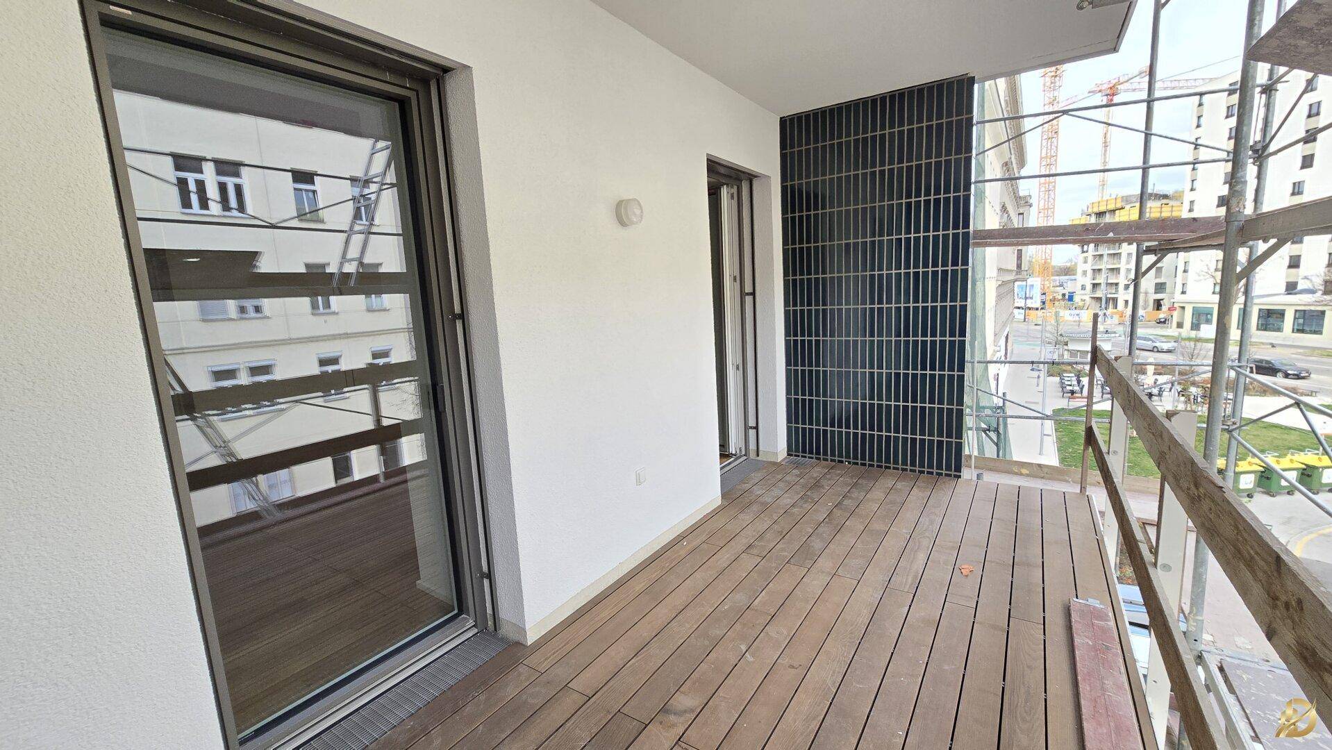 Balkon mit Holzbelag und Zugang zum Innenbereich, umgeben von Baugerüsten.
