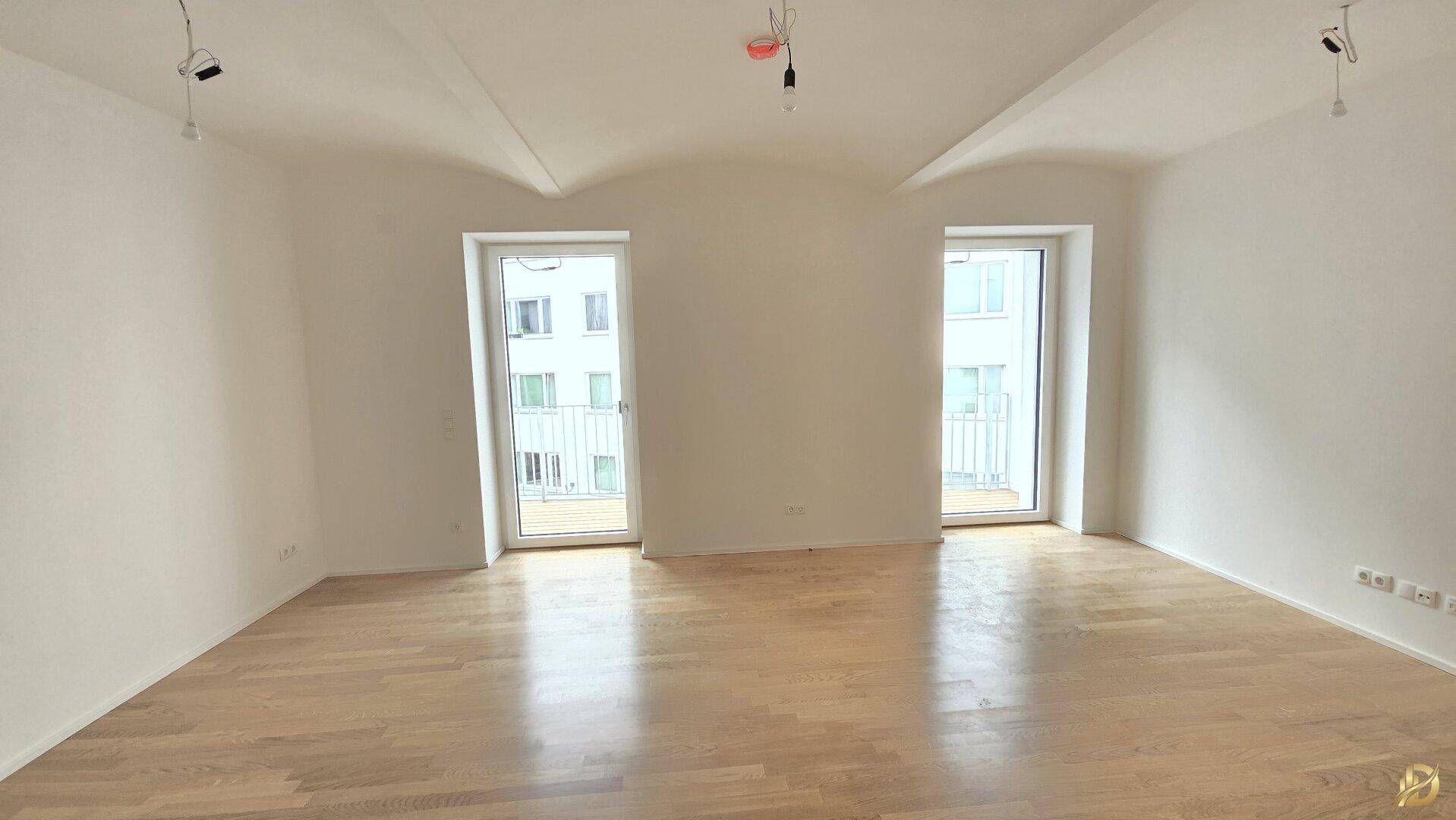 Geräumiges Zimmer mit hellem Holzboden und Zugang zu zwei französischen Balkonen.