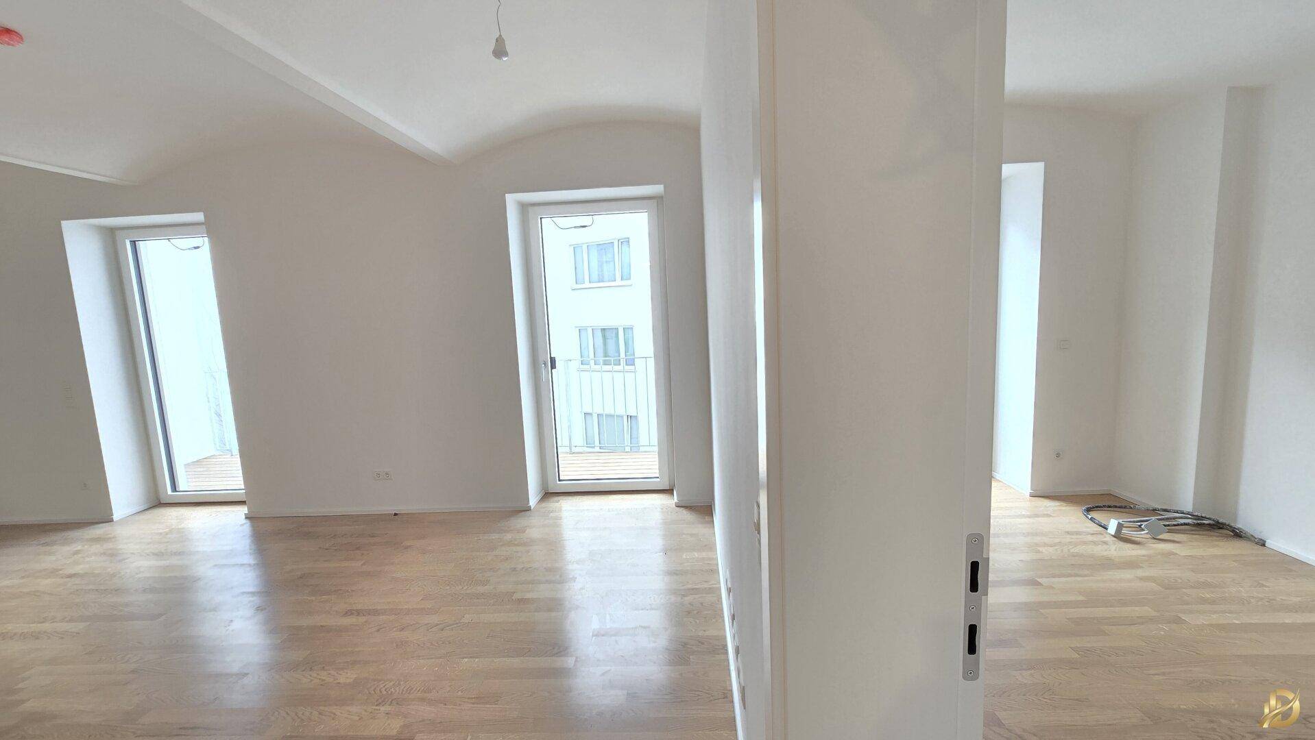 Heller Wohnraum mit Holzboden, einer Säule und zwei französischen Balkonen, ideal für individuelle Gestaltung.