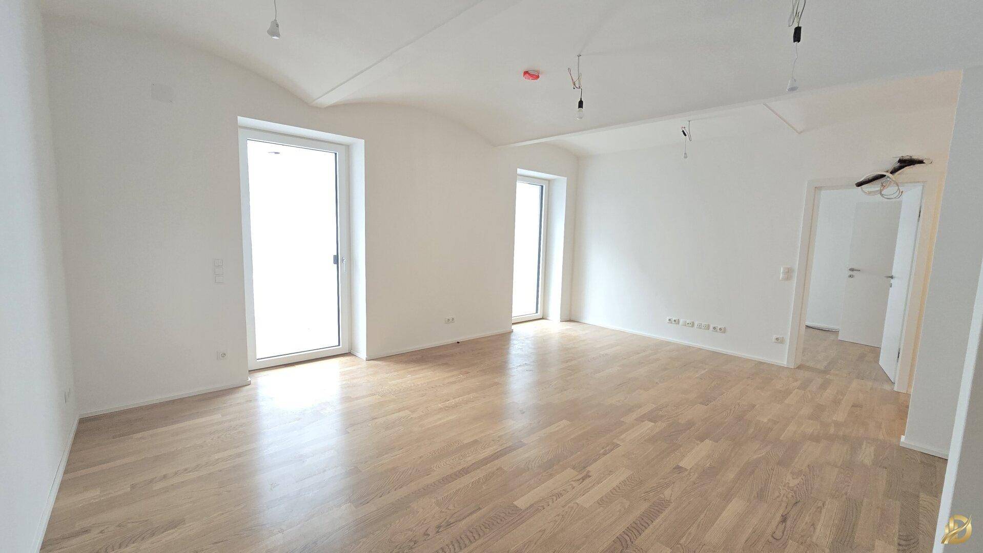 Großzügiges Zimmer mit Parkettboden und zwei Fenstertüren, die viel Tageslicht hereinlassen.
