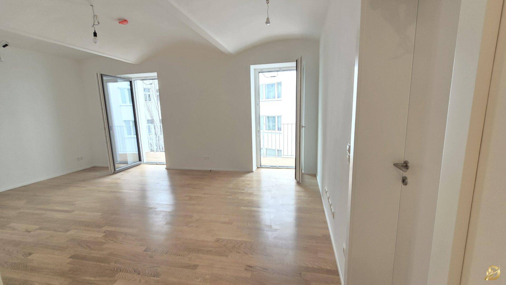 Helles Zimmer mit Holzboden und zwei französischen Balkonen, die viel Licht spenden.