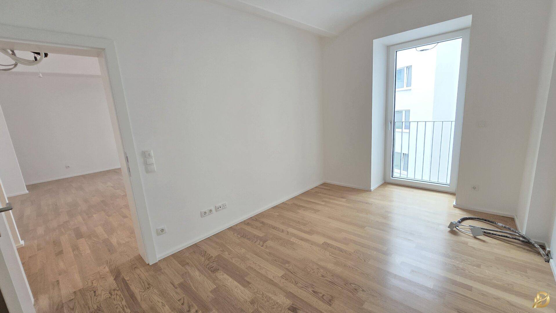 Helles Schlafzimmer mit Parkettboden und einem französischen Balkon, der Tageslicht hereinlässt.