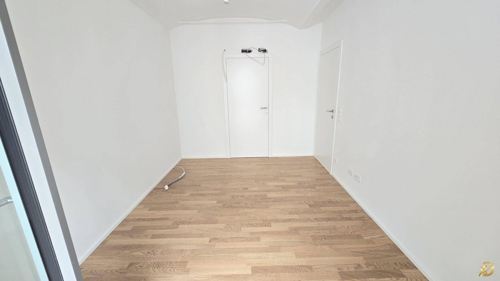 Leeres Zimmer mit Parkettboden und weißen Wänden, bereit für die individuelle Gestaltung.