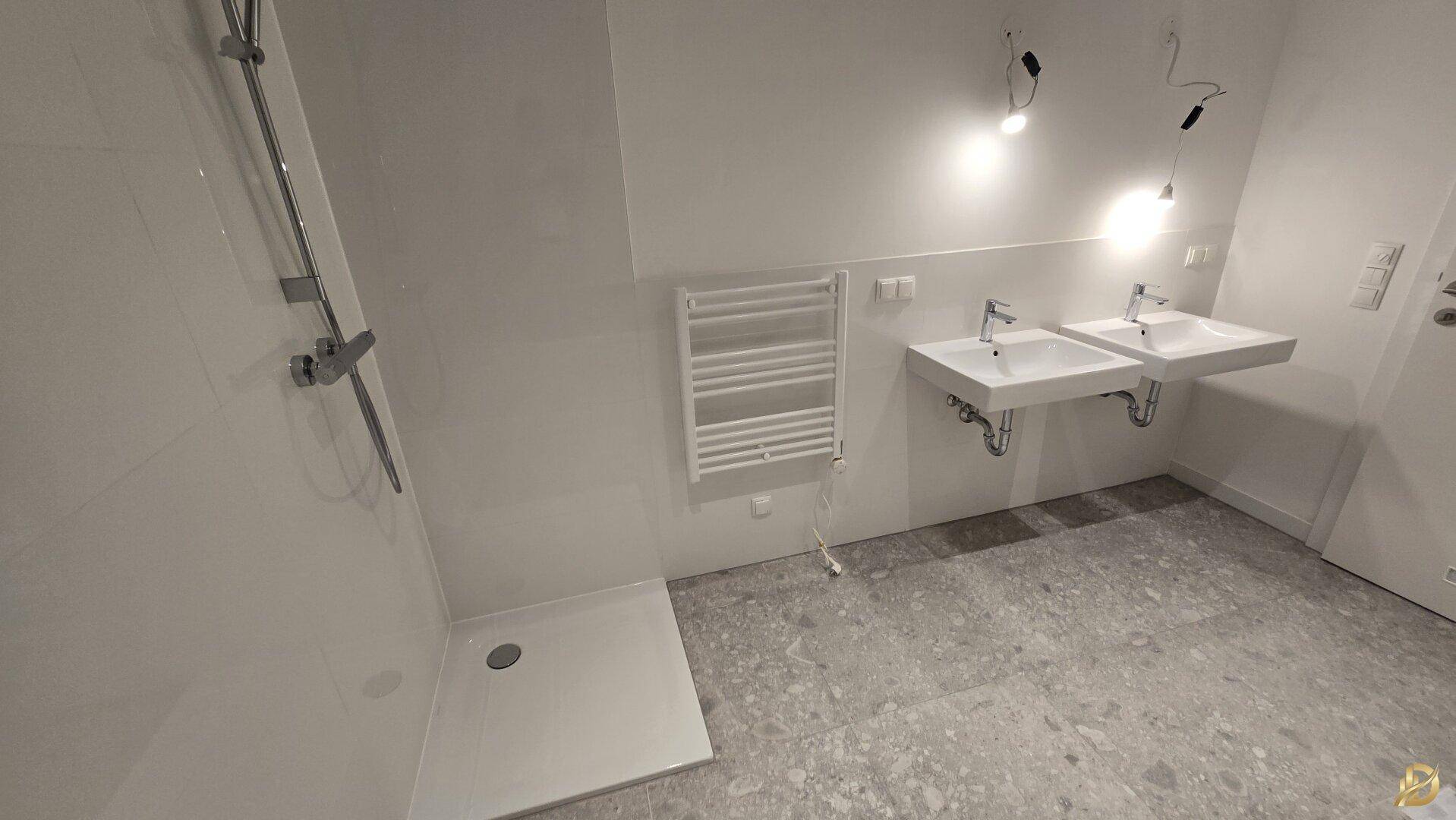 Helles Badezimmer mit ebenerdiger Dusche, Doppelwaschbecken und beheiztem Handtuchhalter.