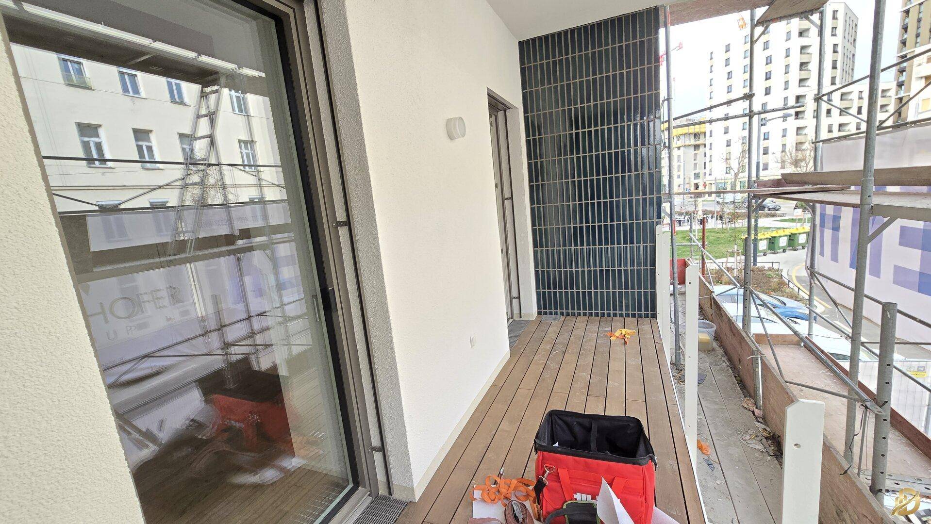Balkon im Bau mit Holzboden und Blick auf die umliegenden Gebäude.
