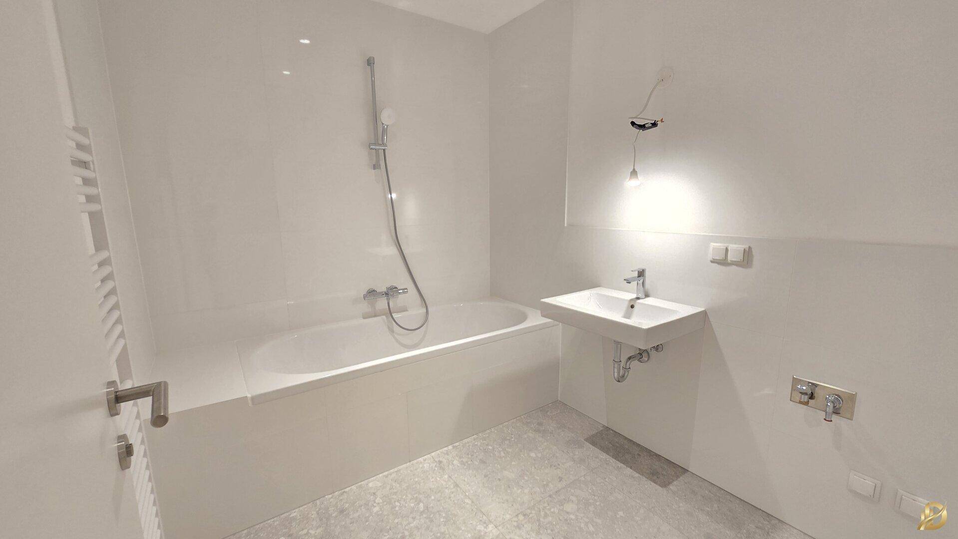 Modernes Badezimmer mit Badewanne, Waschbecken und hellen Fliesen, in neuwertigem Zustand.