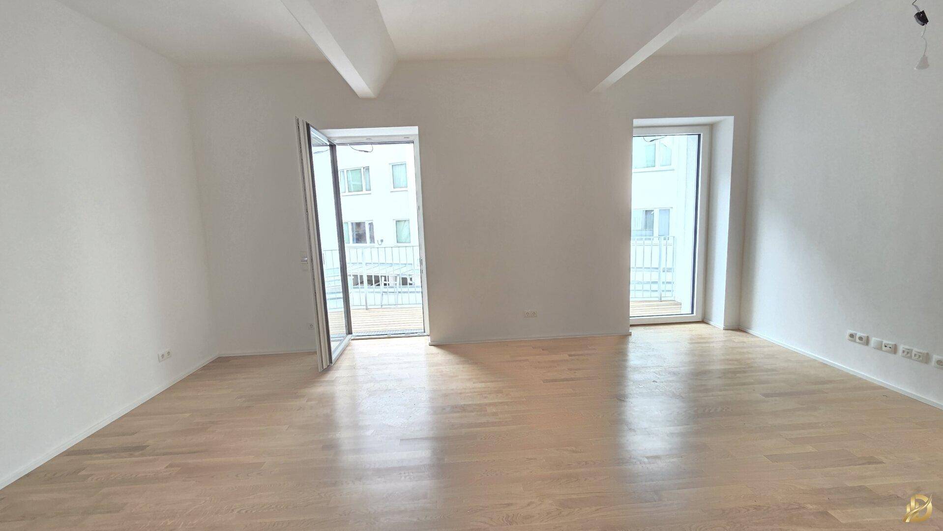 Geräumiges, helles Zimmer mit Holzboden und geöffnetem französischen Balkon.