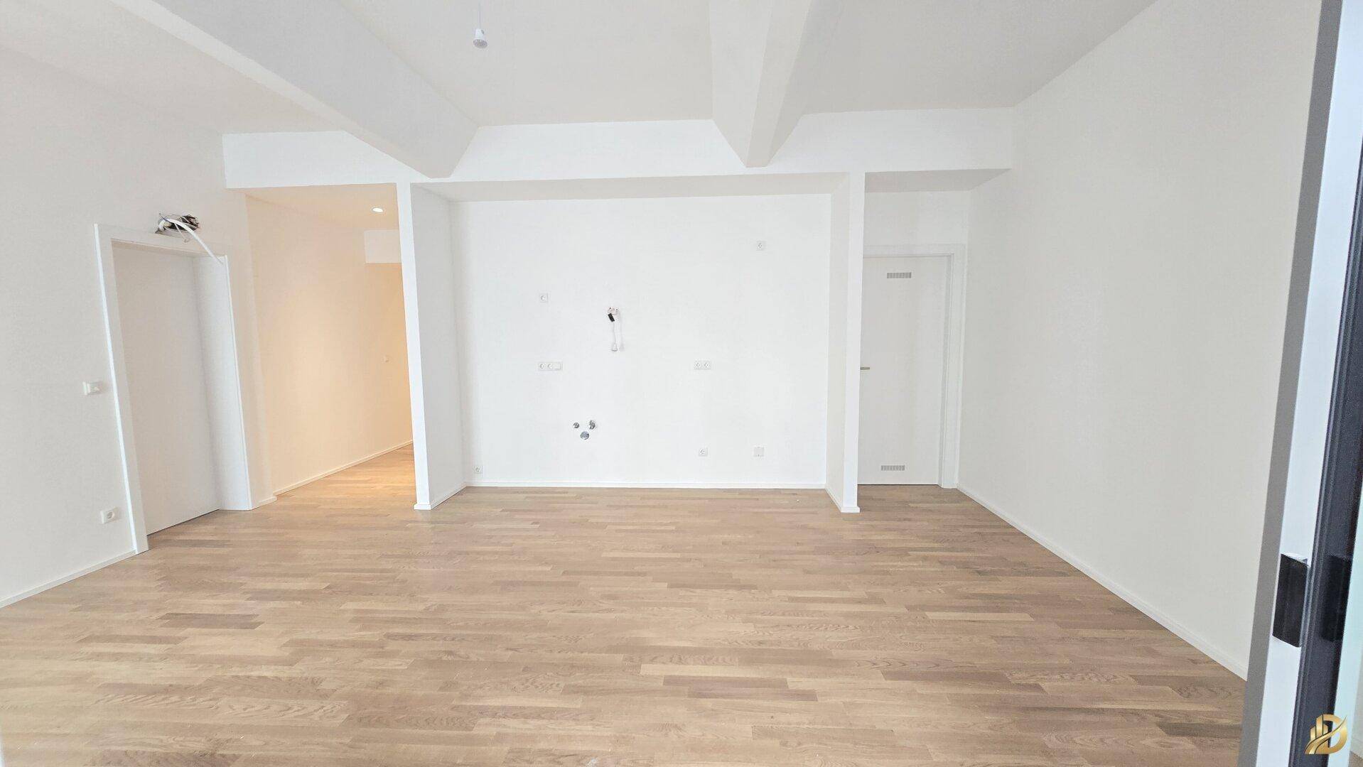 Großes, leeres Zimmer mit Holzboden und weiß gestrichenen Wänden.