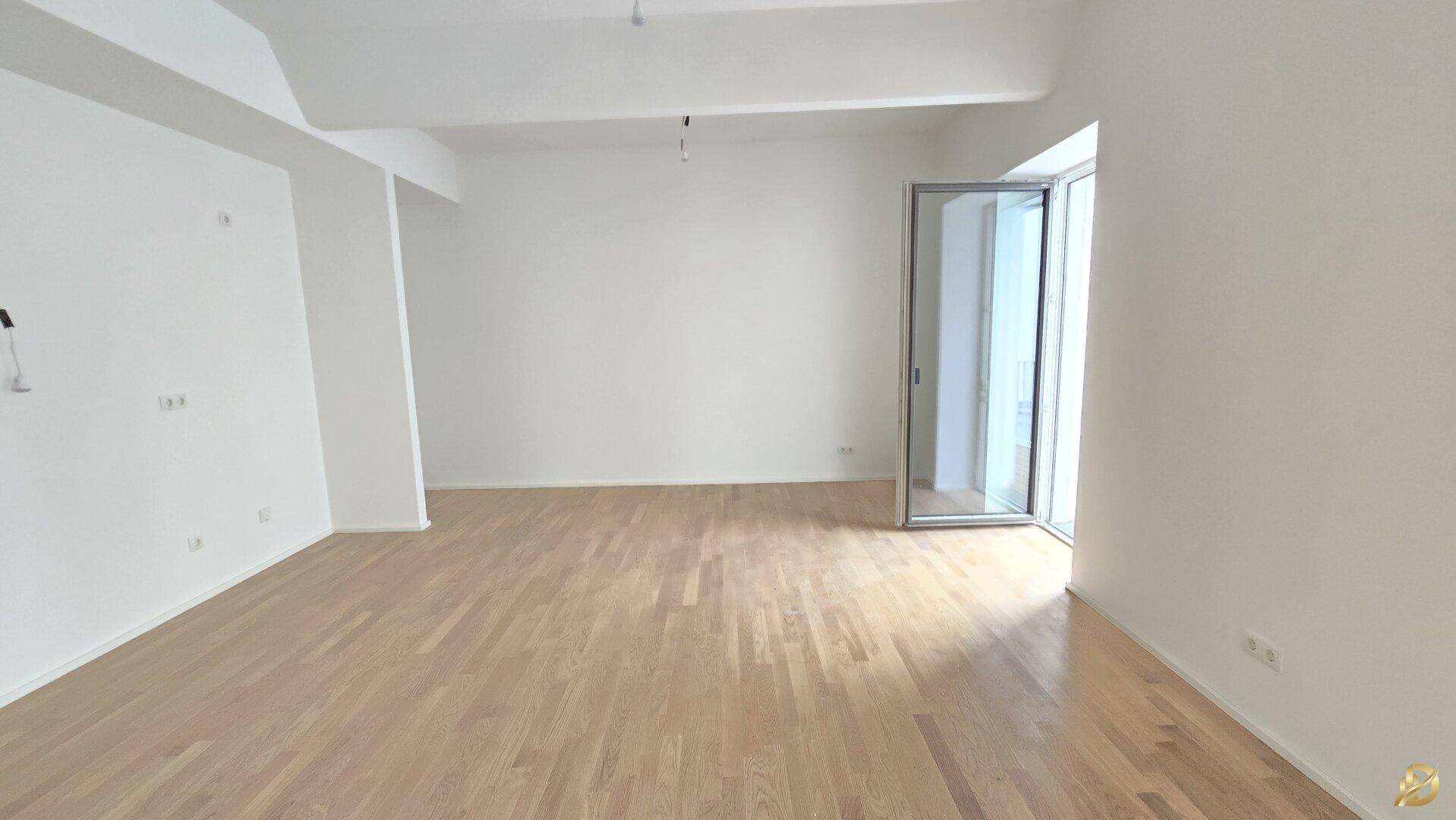 Helles, leeres Zimmer mit Parkettboden und Zugang zu einem französischen Balkon.
