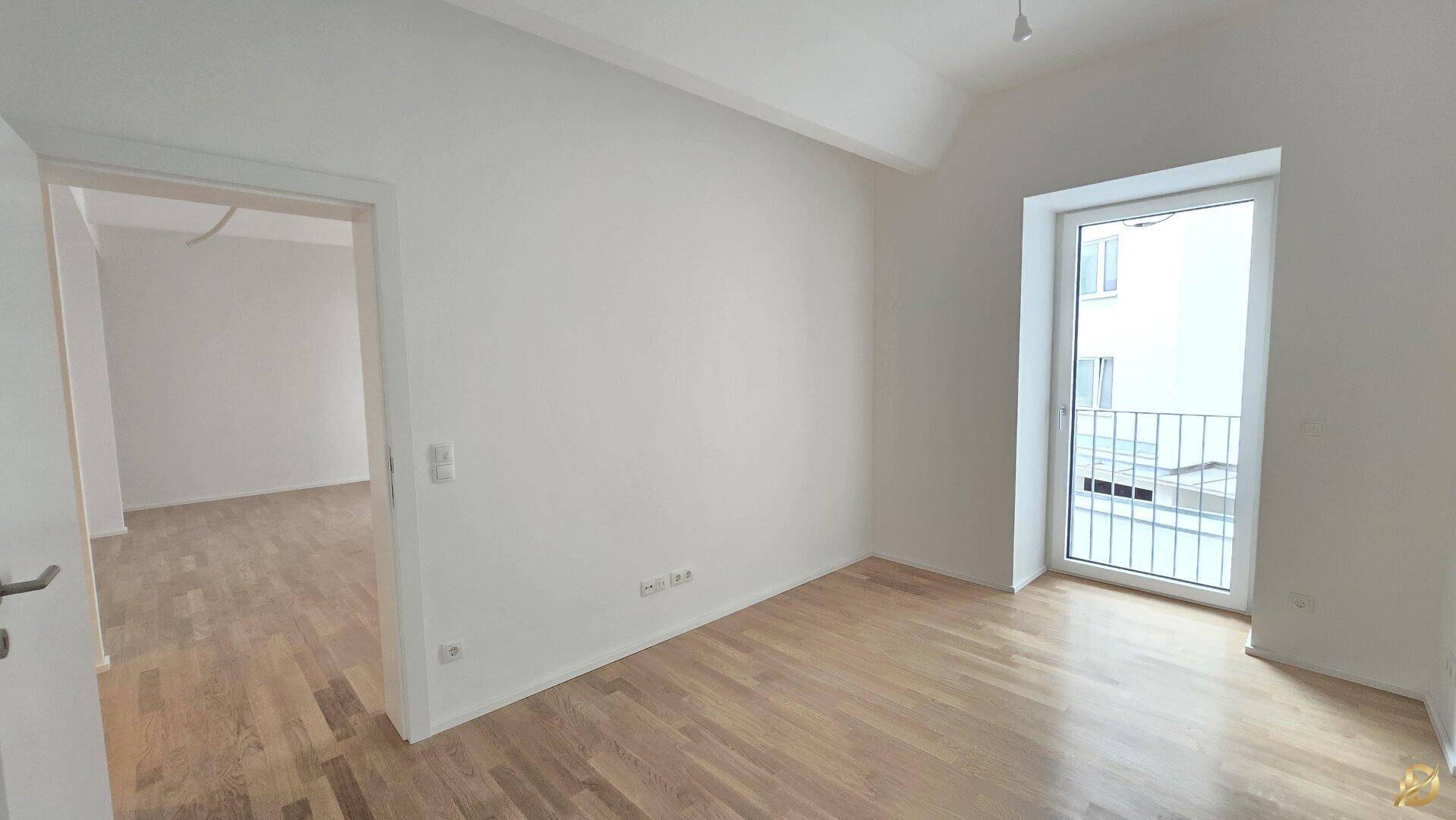 Helles Schlafzimmer mit Parkettboden und Zugang zu einem französischen Balkon.