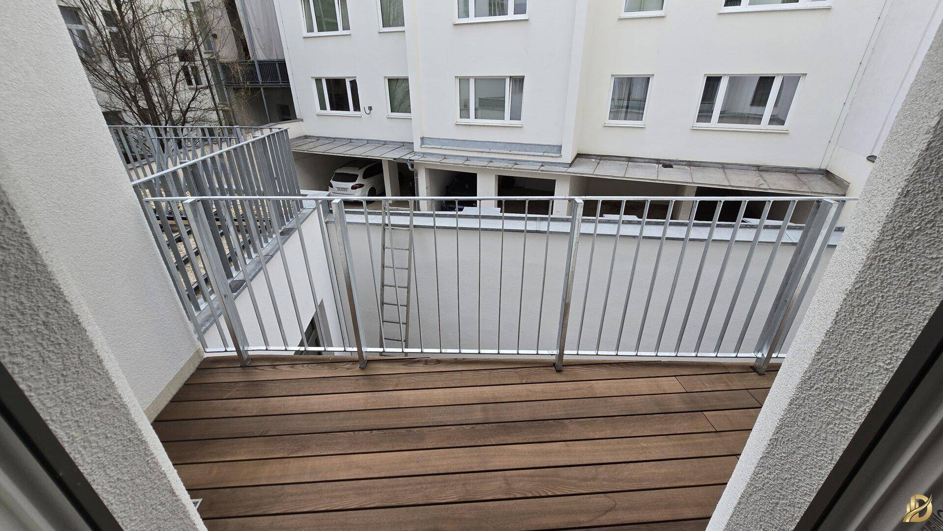 Balkon mit Holzboden und Metallgeländer, Blick auf den Innenhof.
