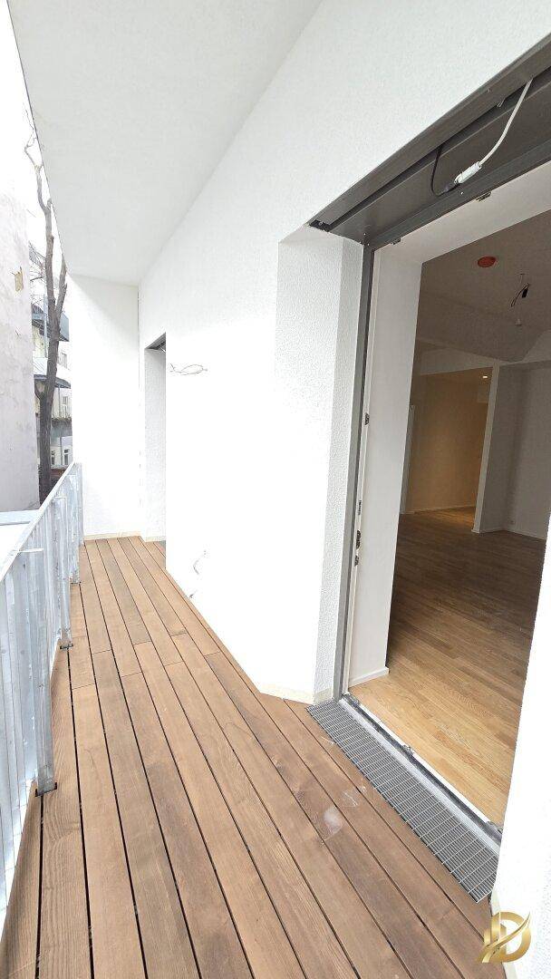 Langer Balkon mit Holzdielen und Zugang zum Innenraum.