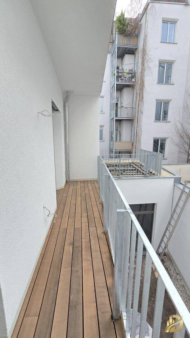 Geräumiger Balkon mit Holzboden und Blick auf die umliegenden Gebäude.