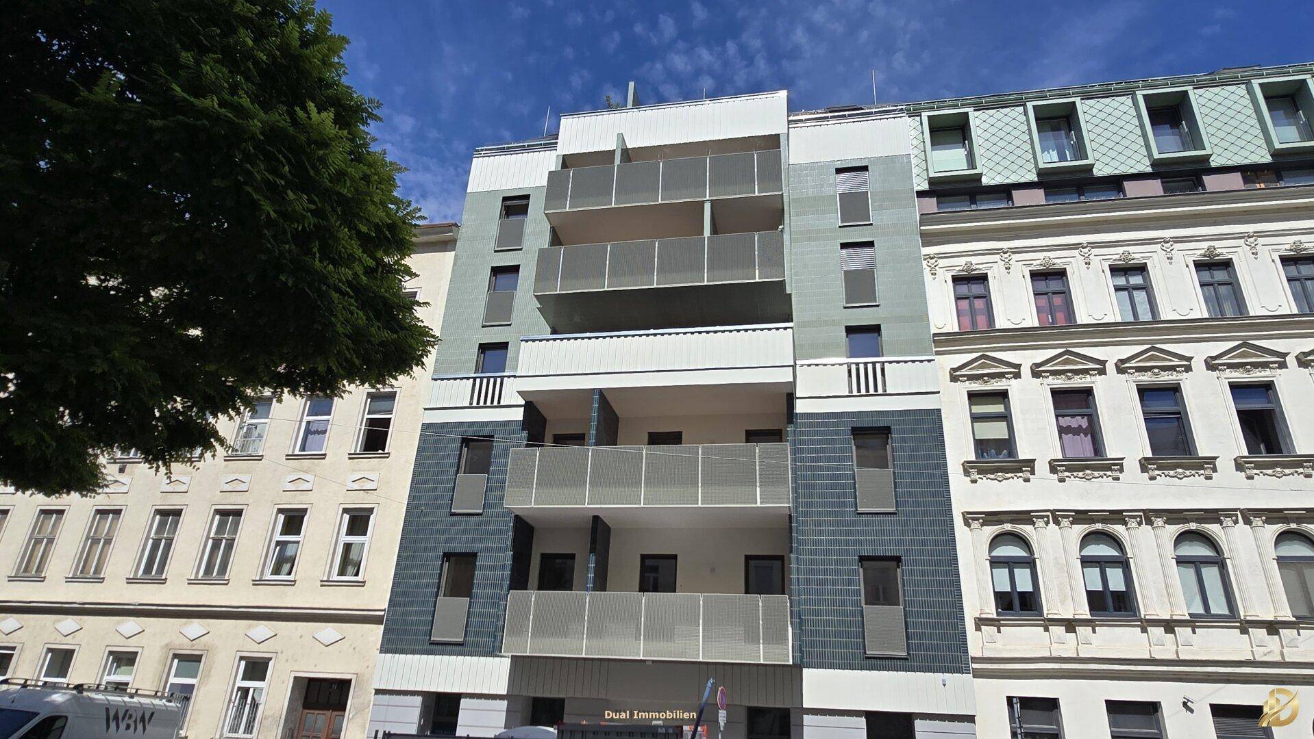 Moderne Wohnhausfassade mit Balkonen und großen Fenstern, umgeben von traditionellen Gebäuden.