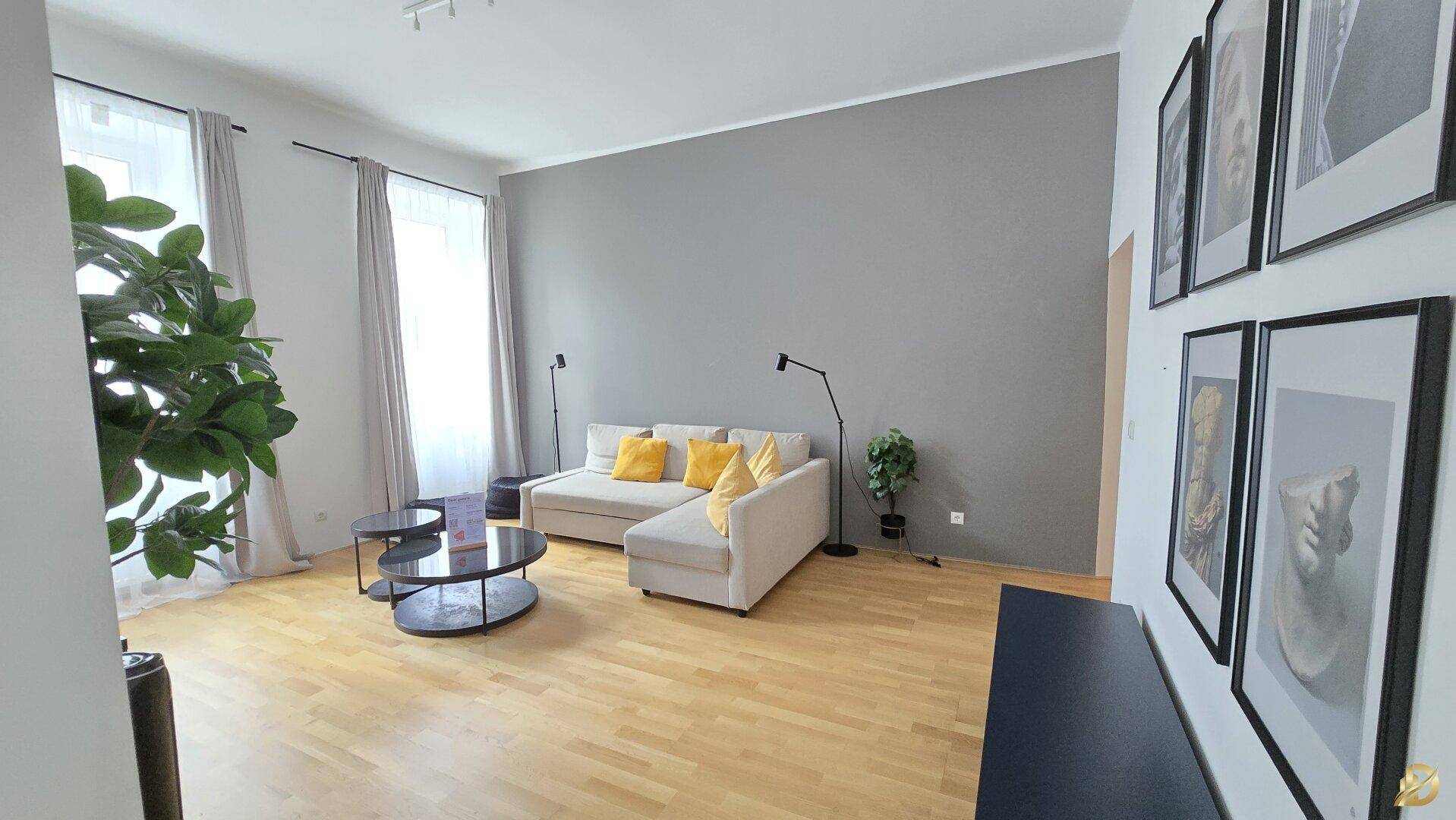 Großzügiges Wohnzimmer mit beigem Ecksofa, Holzboden und Kunstwerken an der Wand.
