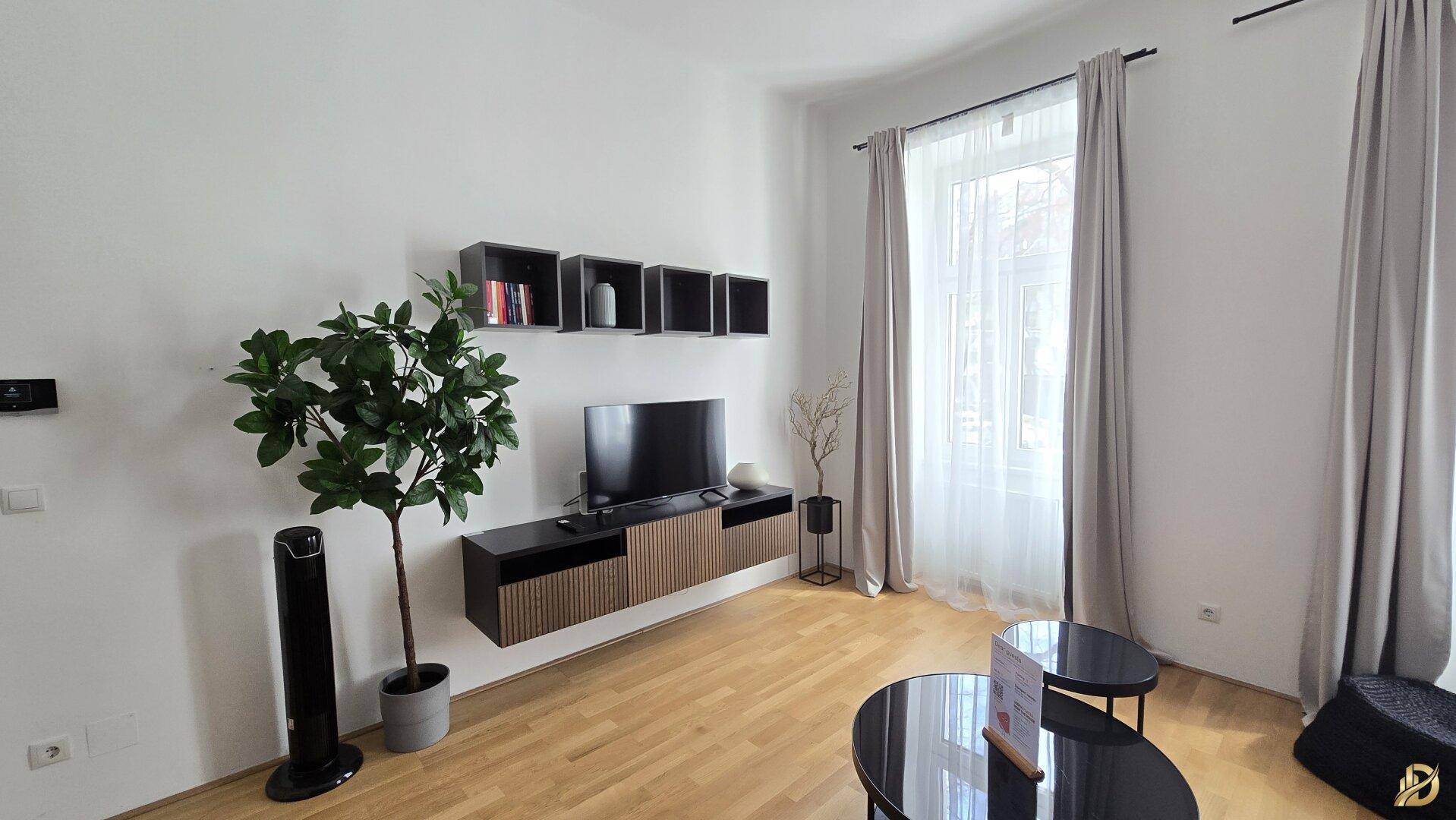 Detailansicht des Wohnzimmers mit großem Fenster, Vorhängen und modernem TV-Möbel.